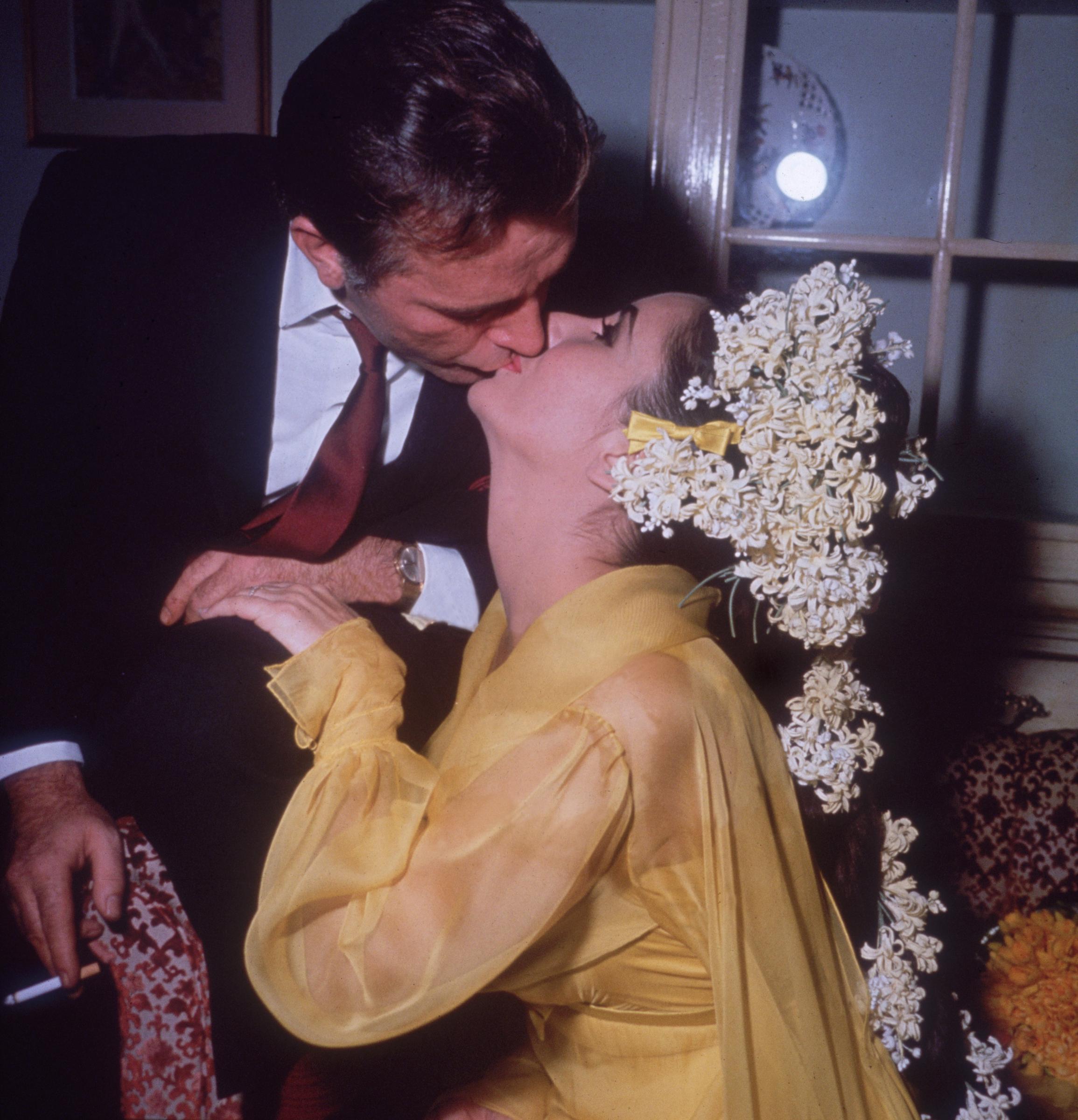 The actress sits on a sofa kissing her fifth husband while he leans over her on their first wedding day, on March 15, 1964 | Source: Getty Images