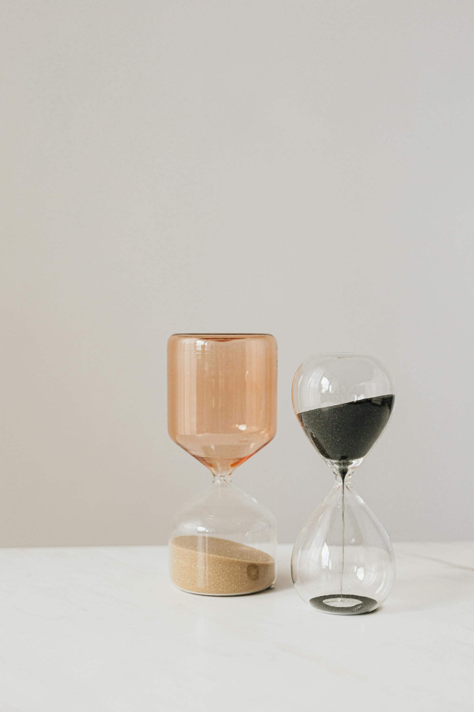 Two modern hourglasses lying on a white surface | Source: Pexels