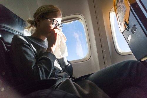 Une jeune femme éternuant dans un avion | Photo : Shutterstock Une jeune femme éternuant dans un avion | Photo : Shutterstock