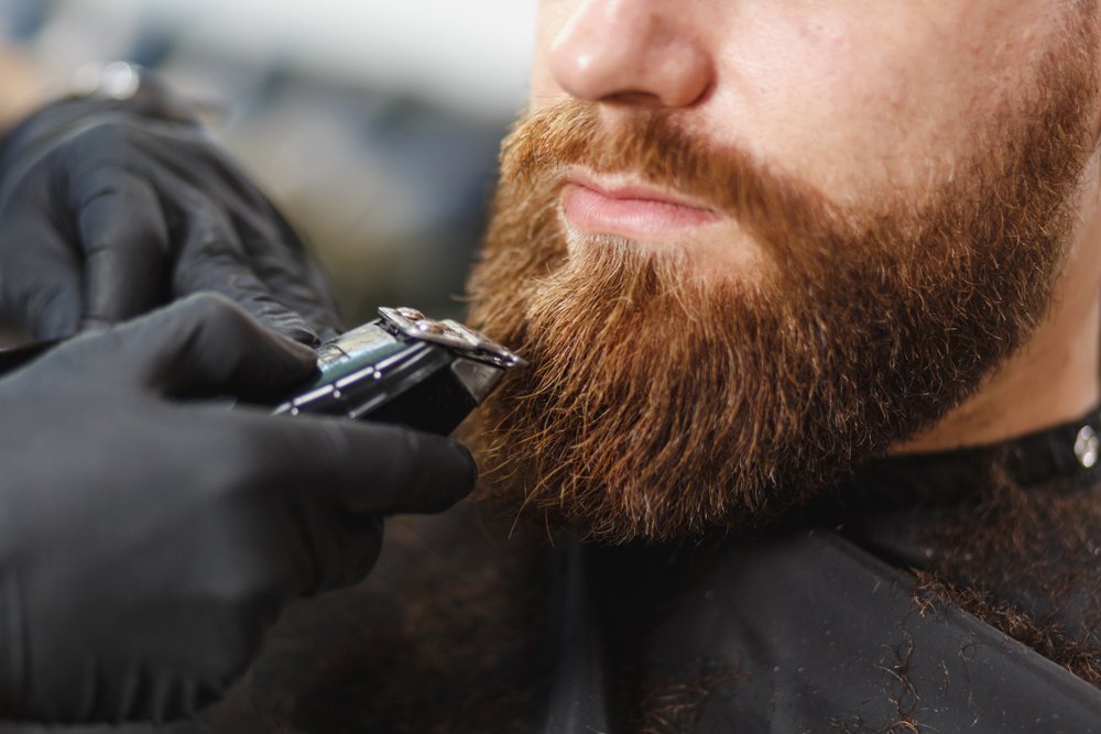 Un homme se faisant tailler la barbe à l'aide d'une tondeuse. | Photo : Shutterstock