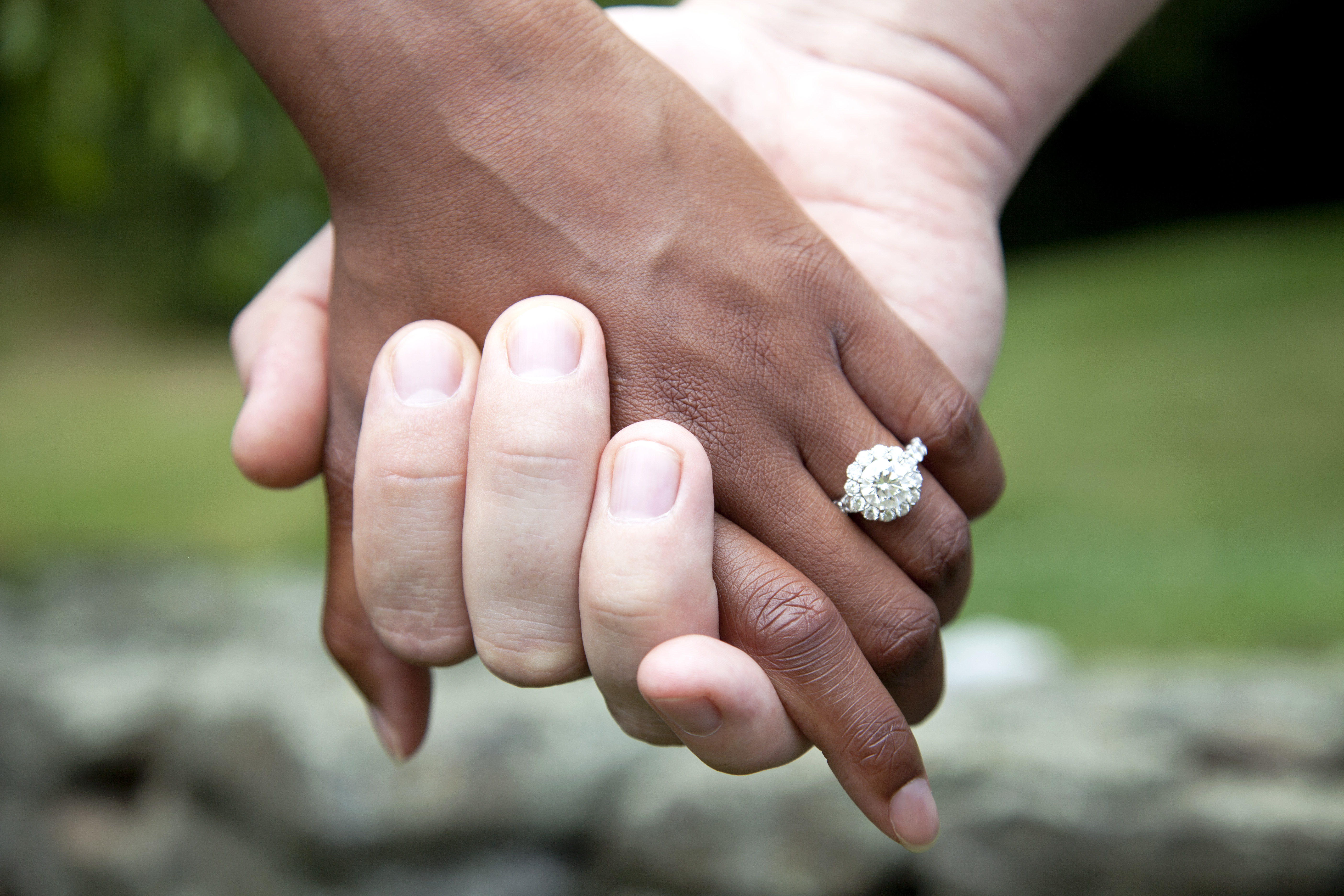 Interracial Couple Holding Hands and Diamond Engagement Ring, Close-Up | Source: Getty Images
