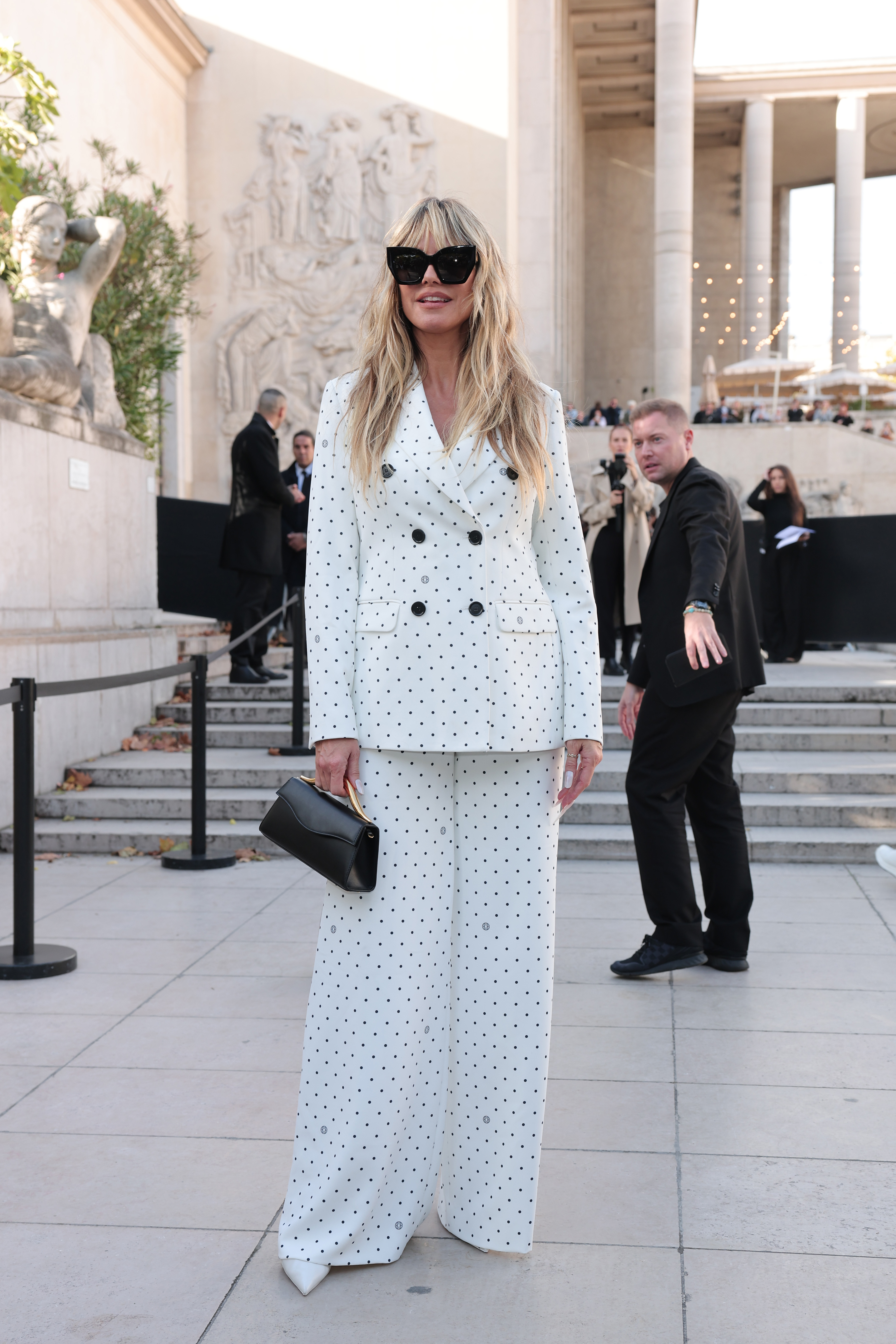 Still at the Elie Saab Womenswear Spring/Summer 2026 show held on October 4, 2025, Heidi Klum accessorized her pantsuit with large black-tinted sunglasses and a sleek black purse. She completed the look with a pair of white towering stilettos.