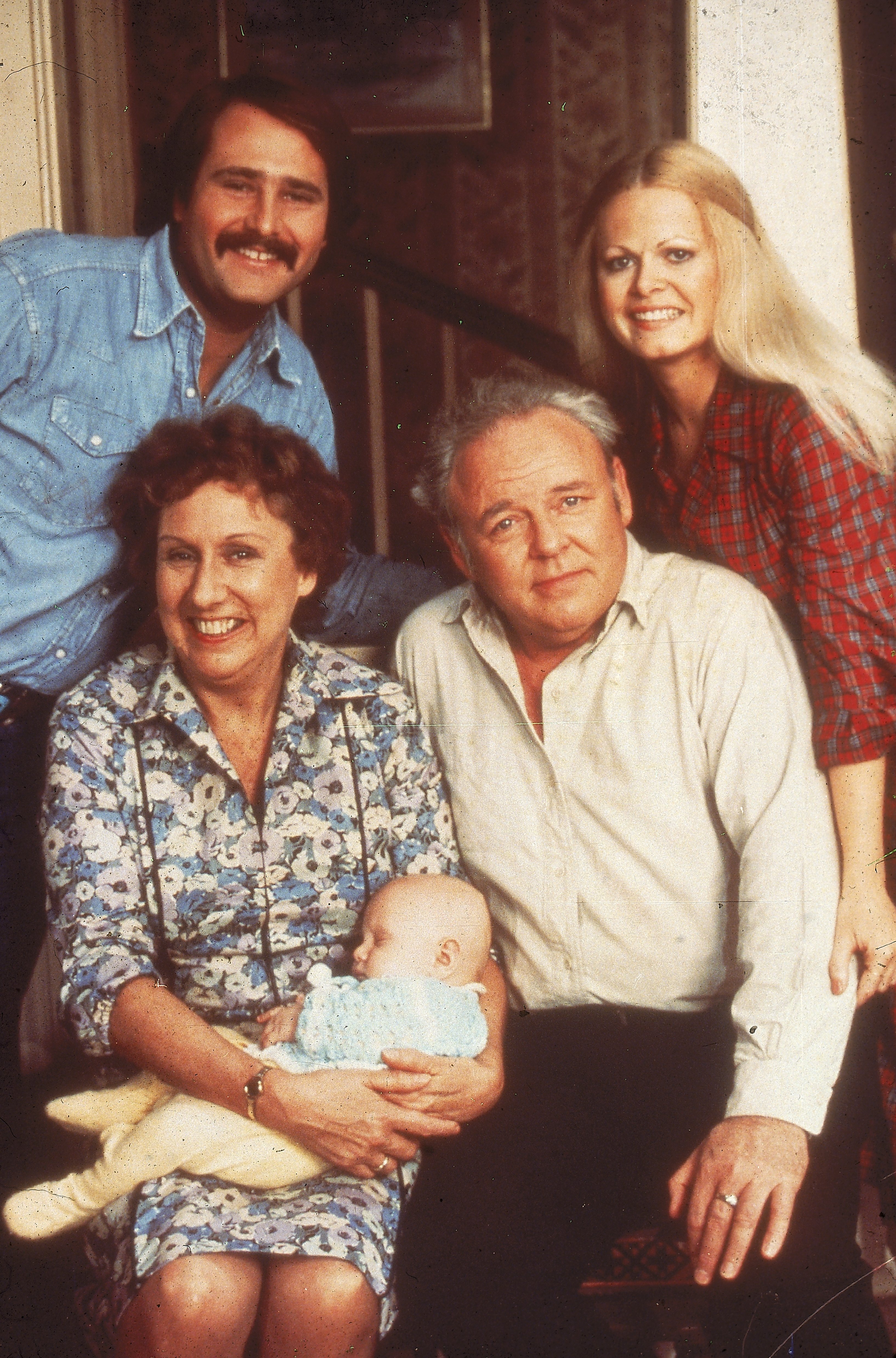 Portrait of the cast of the TV show 'All in the Family'.  Clockwise from bottom right: Carroll O'Connor (1924 - 2001), Jean Stapleton holding Corey M Miller, Rob Reiner and Sally Struthers.  |  Source: Getty Images