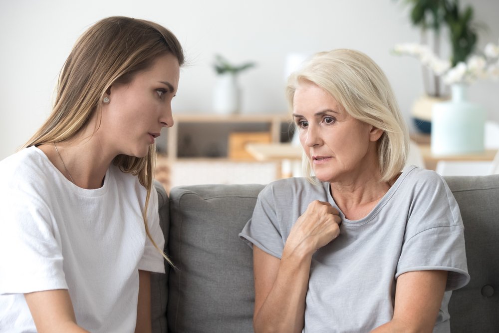 Concerned aged mother and adult daughter sit on couch having serious conversation. | Photo: Shutterstock