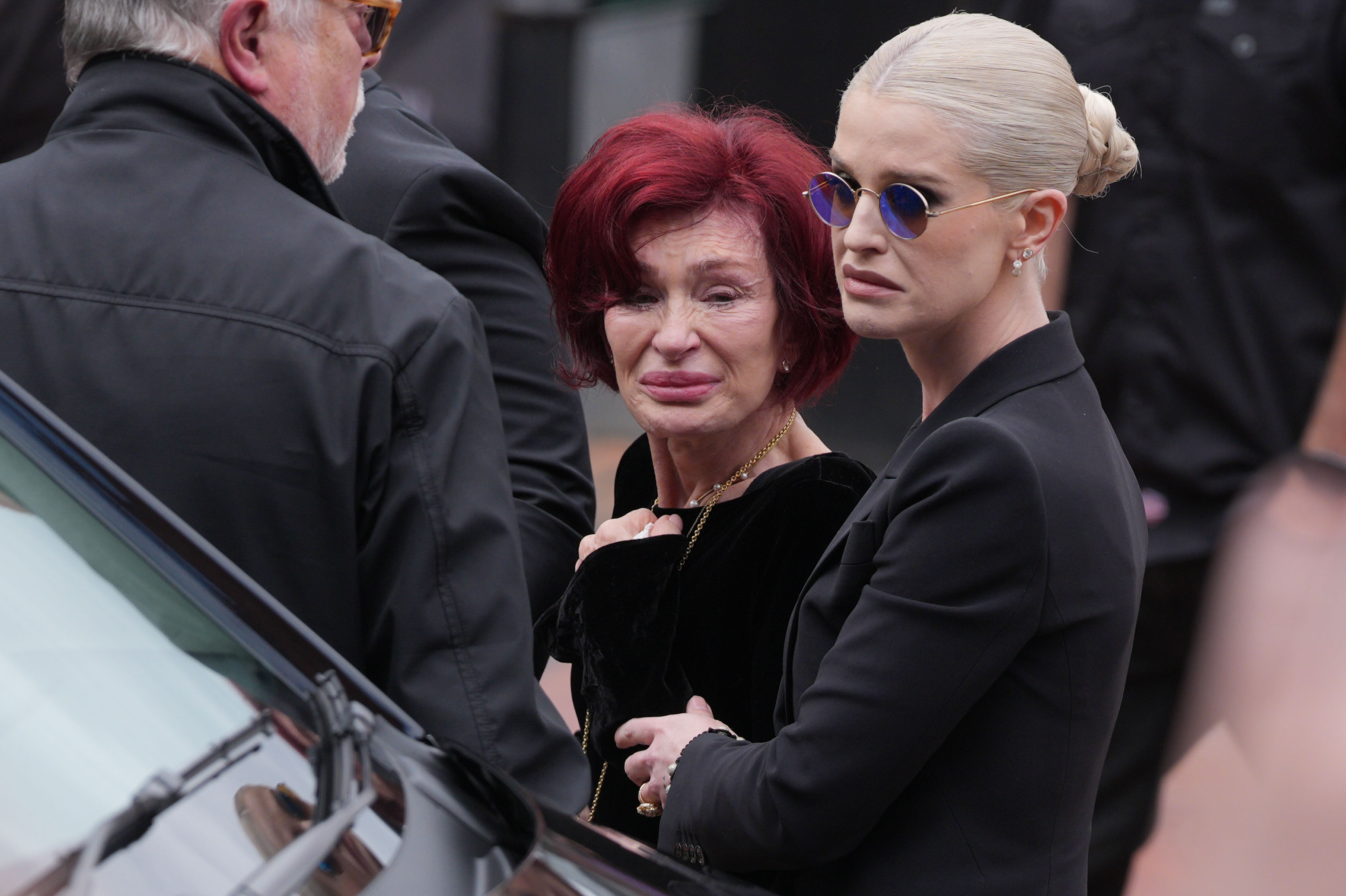 Sharon and Kelly Osbourne stop to view tributes from fans to the late rockstar at Black Sabbath Bench and Bridge as his funeral cortege travels through his home city of Birmingham.