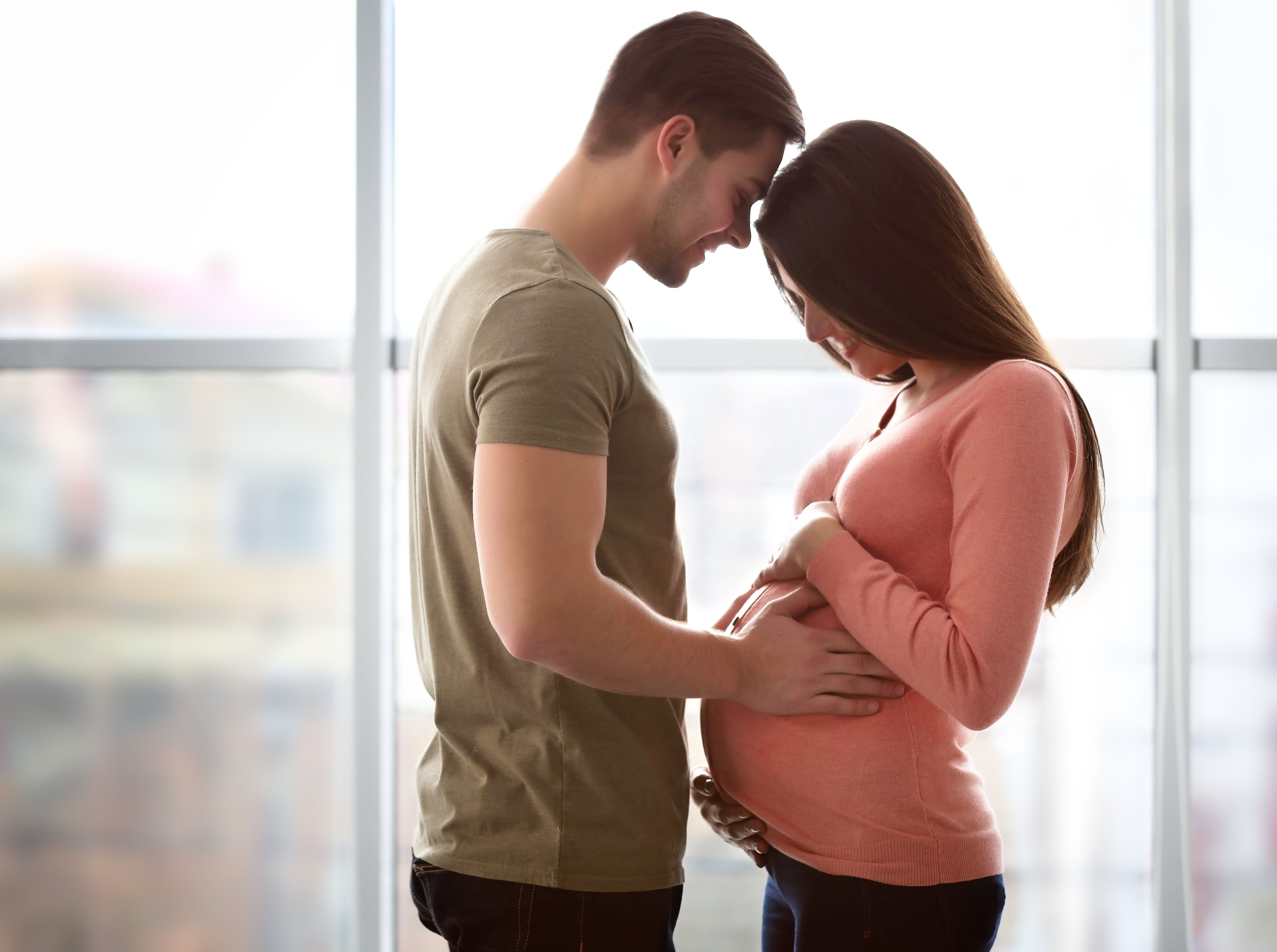A woman looking down at her pregnant belly as her husband rests his forehead on hers | Source: Shutterstock