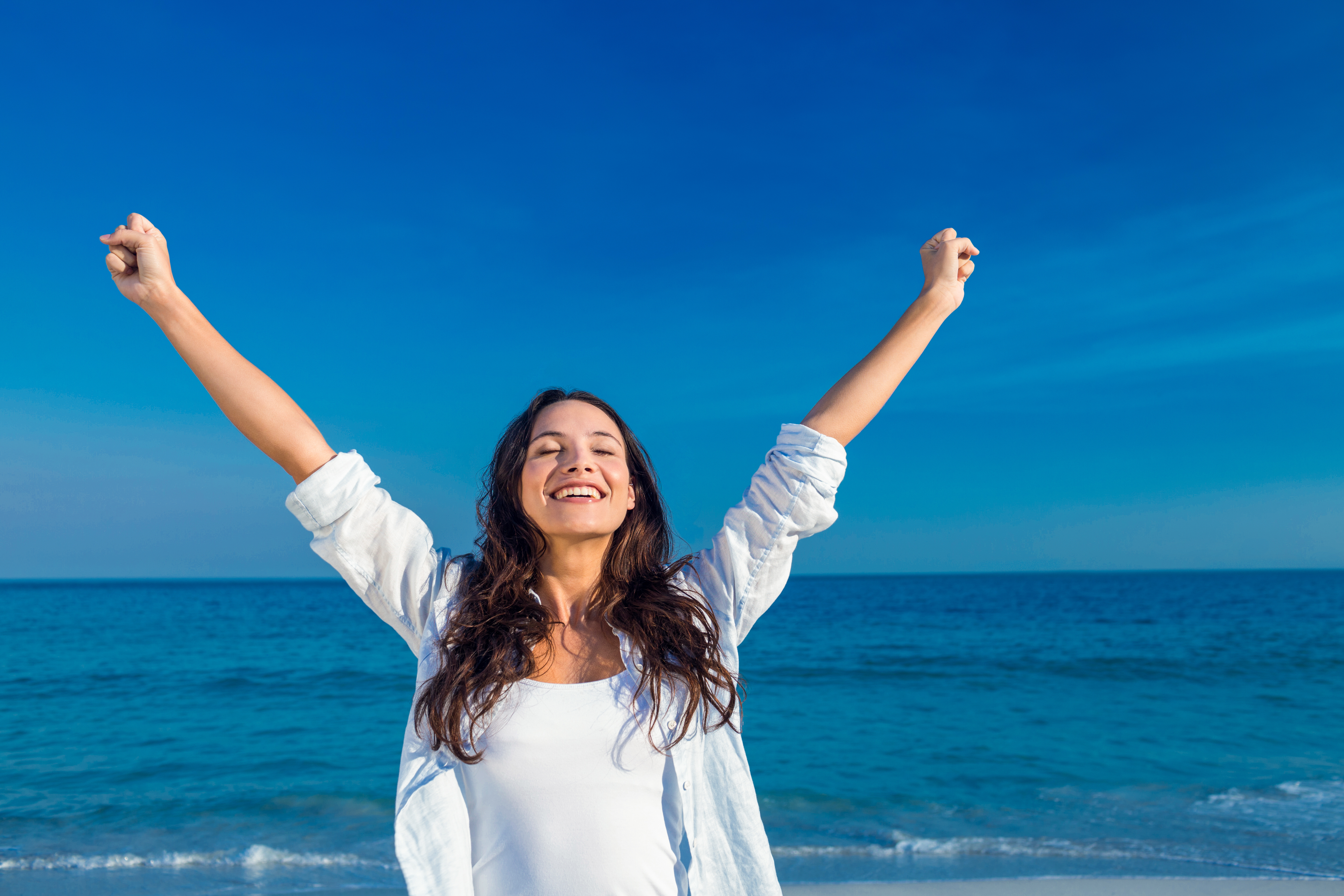 A woman smiling with her hands raised above her head on the beach | Source: Shutterstock