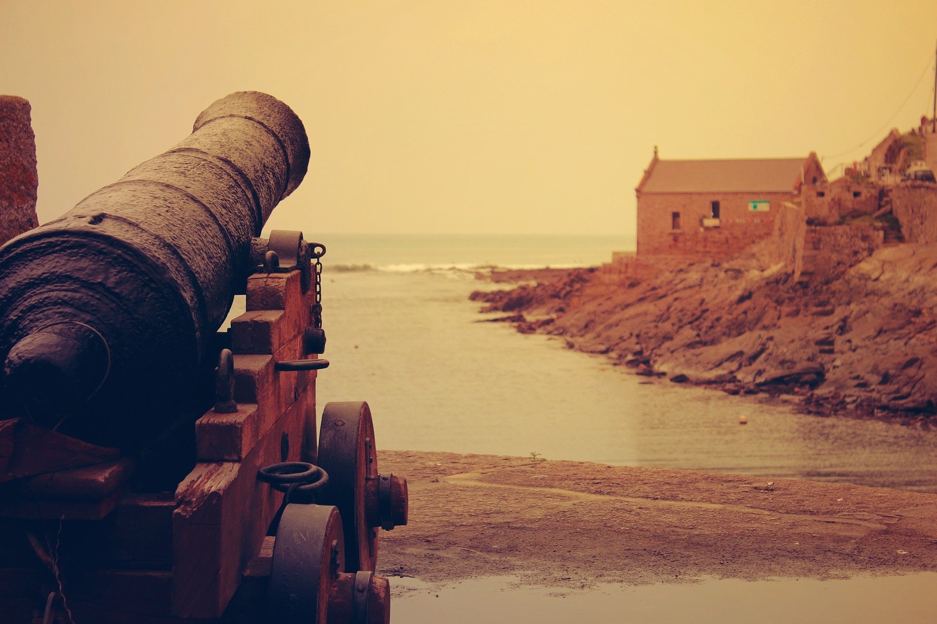 A cannon facing the seashore with a house in the distance | Photo: Pixabay/Free-Photos