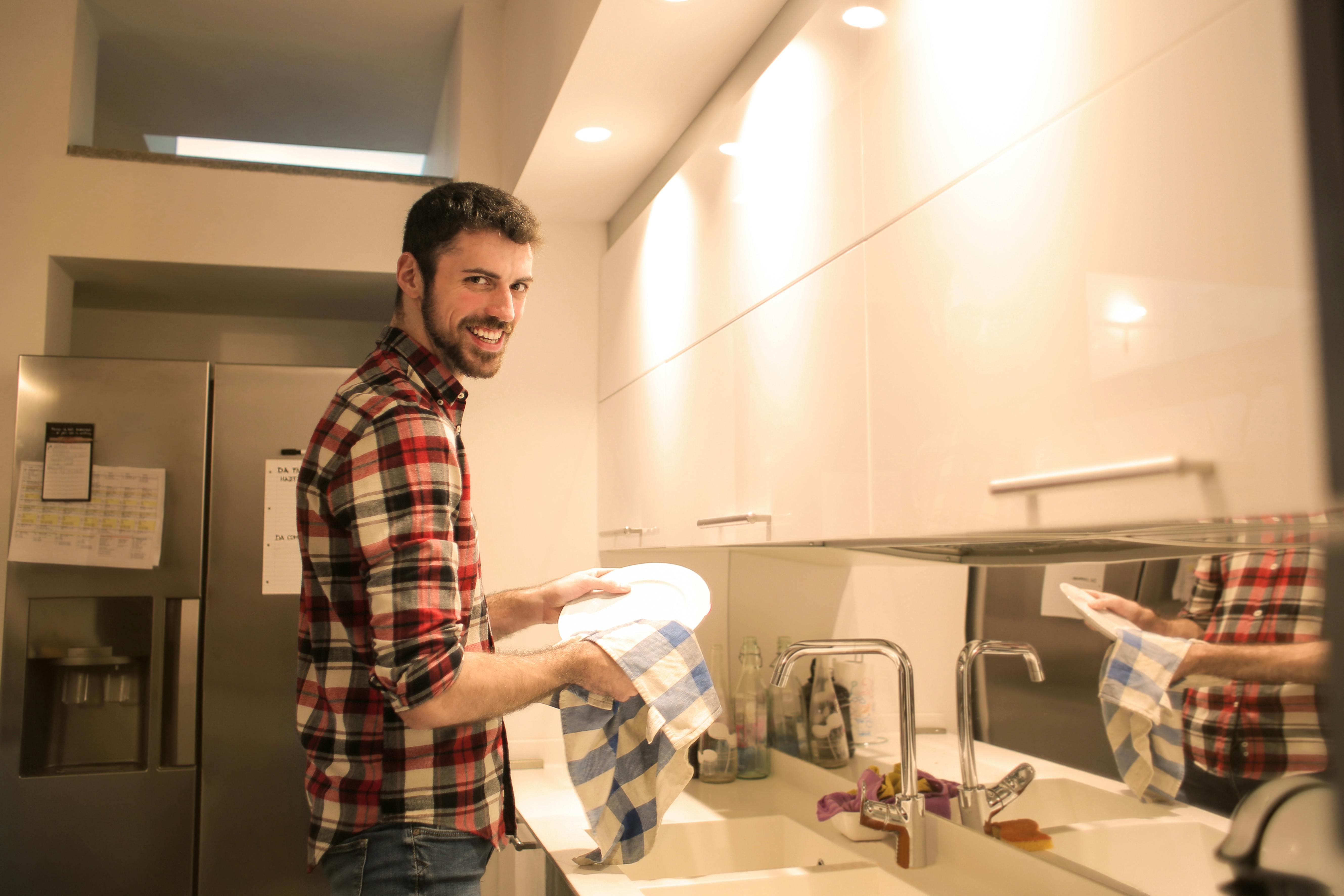 Man smiling as he does the dishes | Source: Pexels