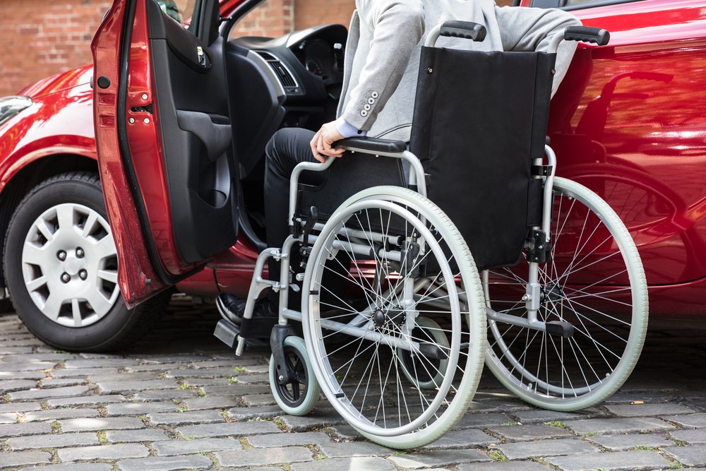 Junger behinderter Mann, der neben seinem Auto auf der Straße sitzt. I Quelle: Shutterstock