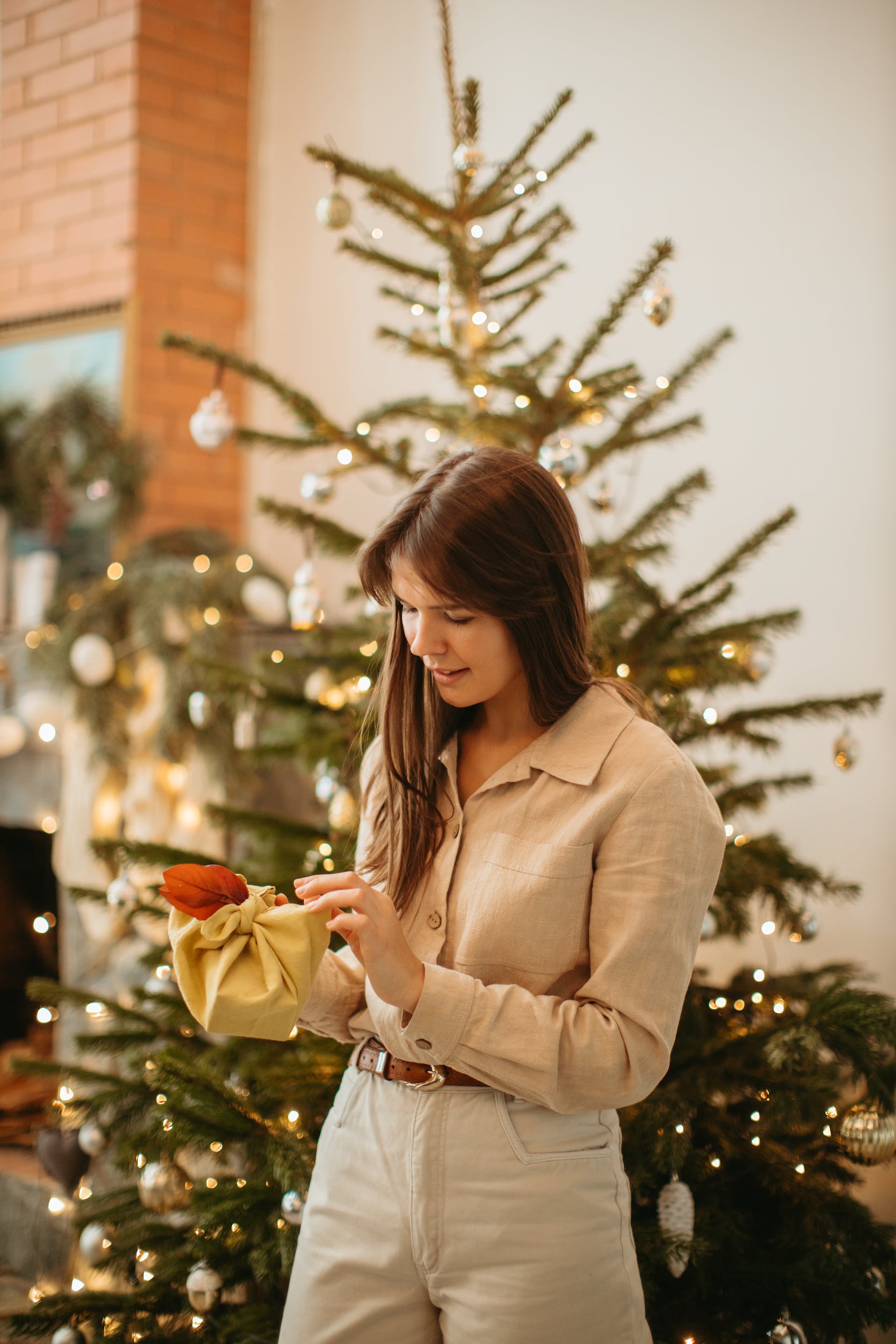 A woman holding a gift box while standing near a Christmas tree | Source: Pexels