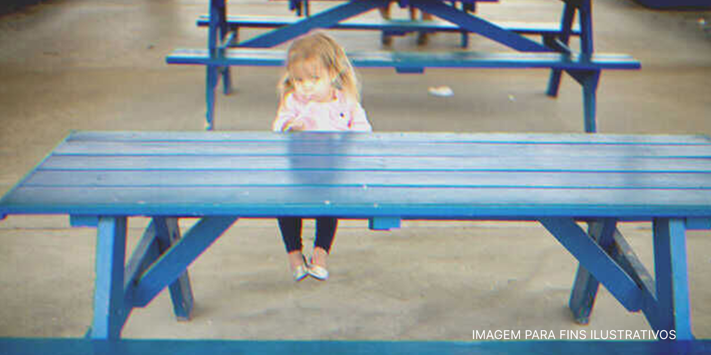 Menina sentada frente a uma mesa azul. | Foto: Shutterstock
