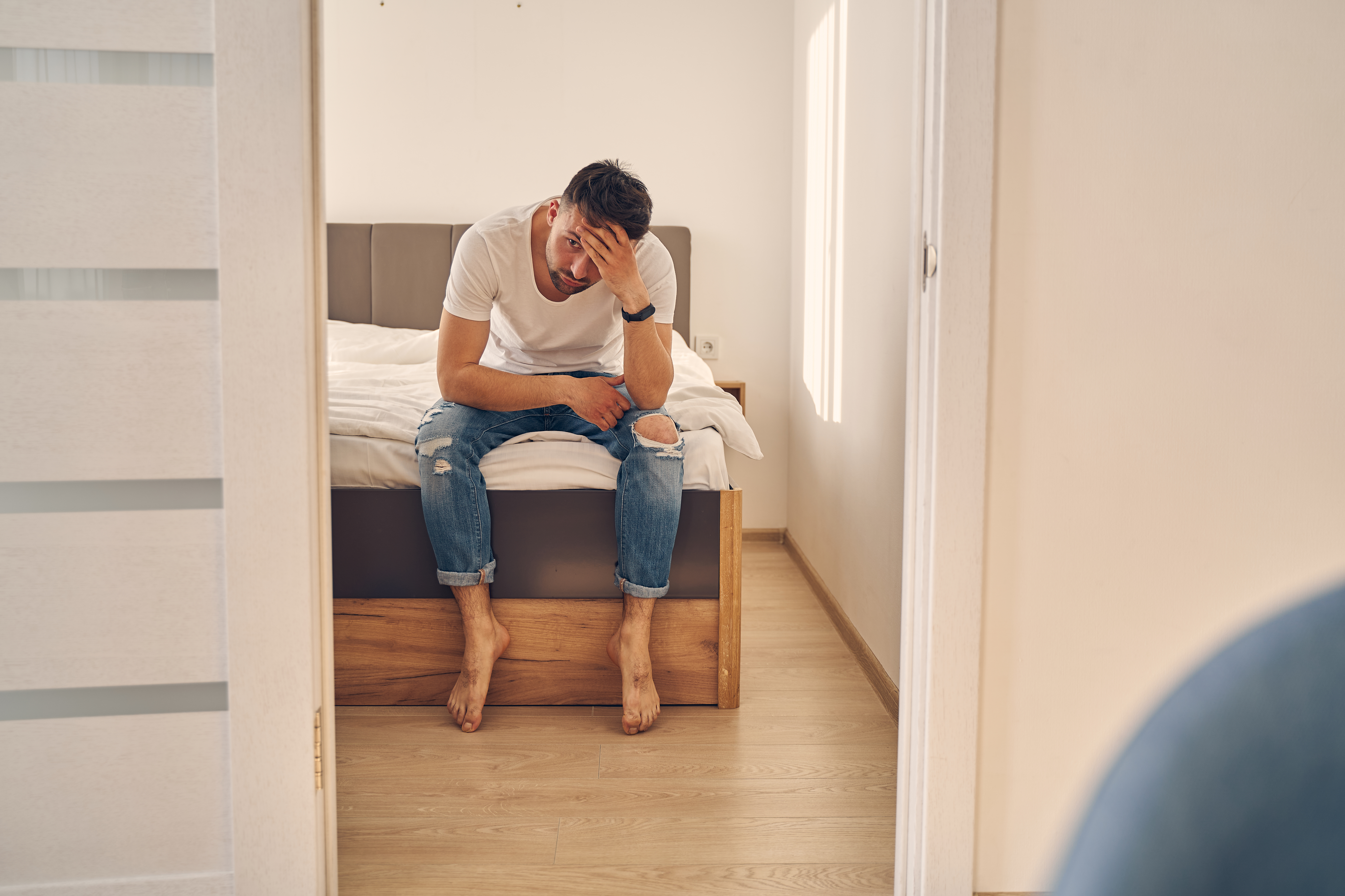 An anxious Caucasian man is seen spending time at home in the bedroom while thinking of his problems | Source: Shutterstock