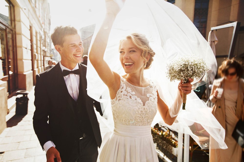 Un novio feliz junto a la novia mientras ella sostiene el velo sobre su cabeza. | Foto: Shutterstock