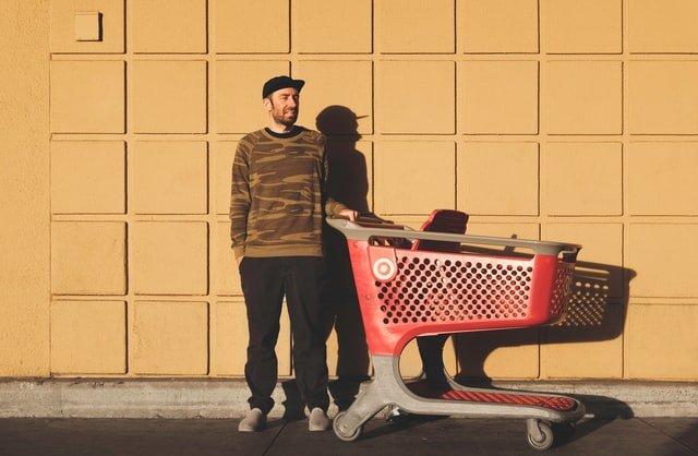 Man with shopping cart stands against a wall outside | Photo: Unsplash