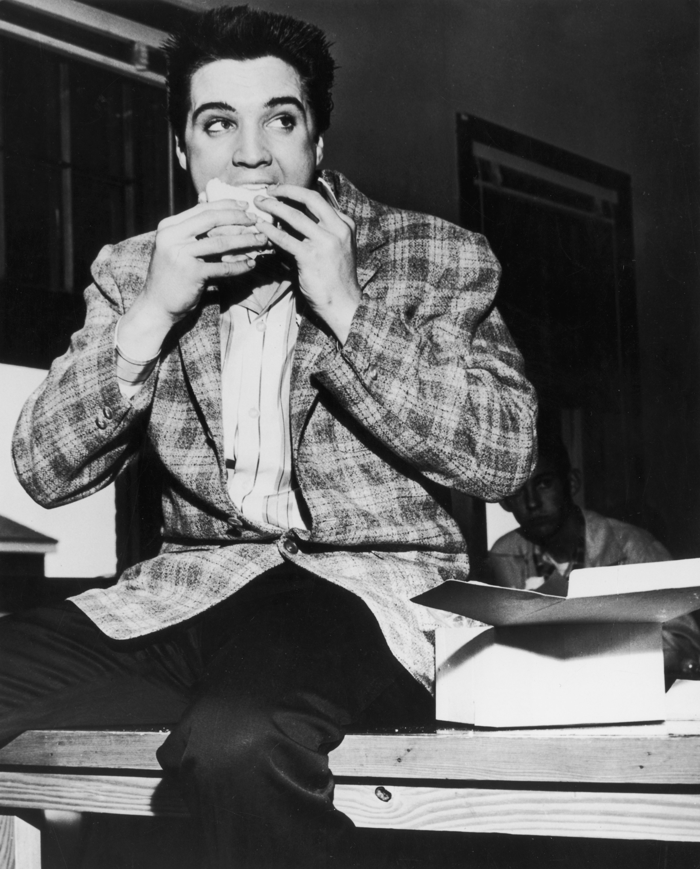 Actor Elvis Presley pictured sitting on a bench eating a sandwich on March 25, 1958 in Memphis, Tennessee ┃ Source: Getty Images