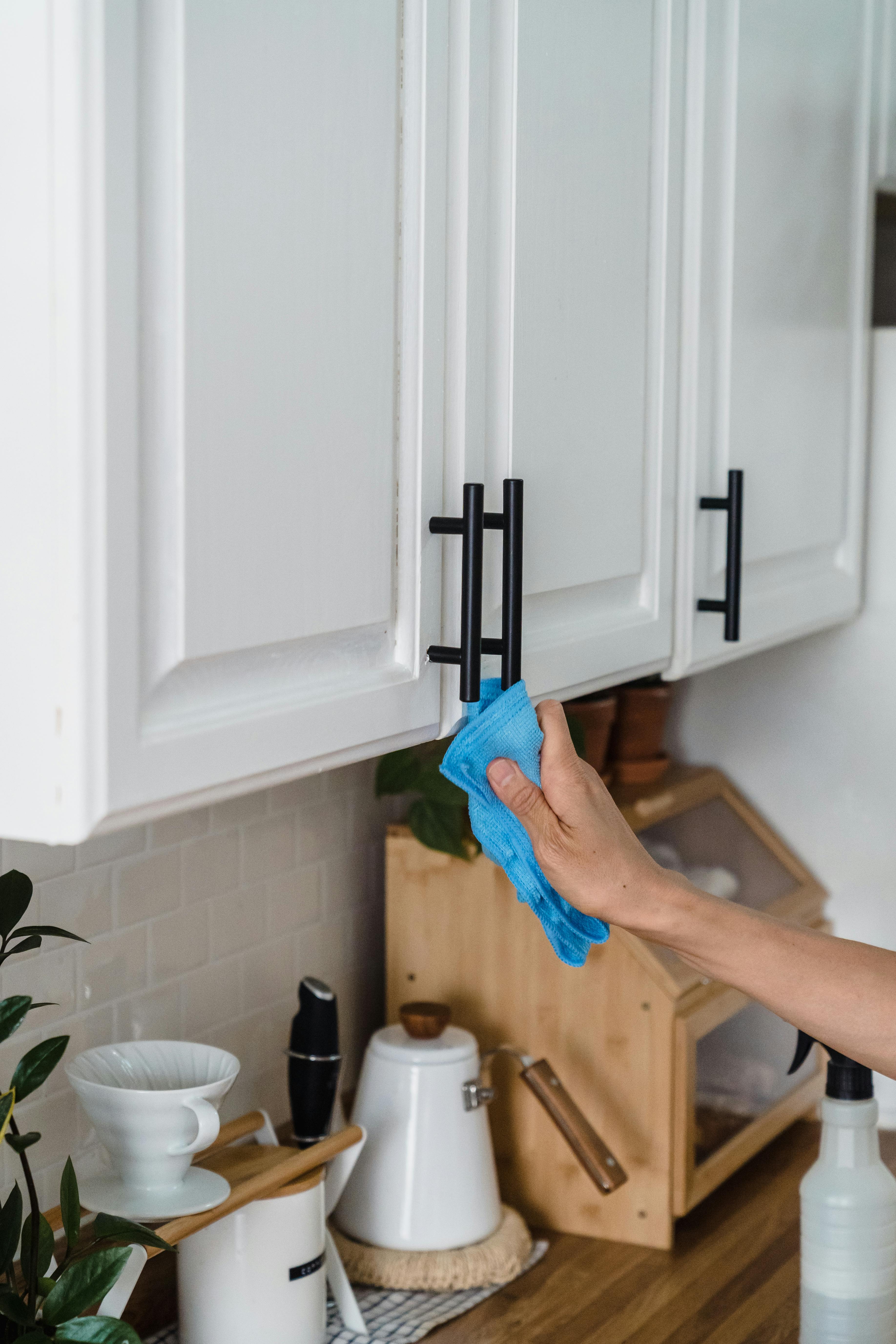 A person wiping down kitchen cabinets | Source: Pexels