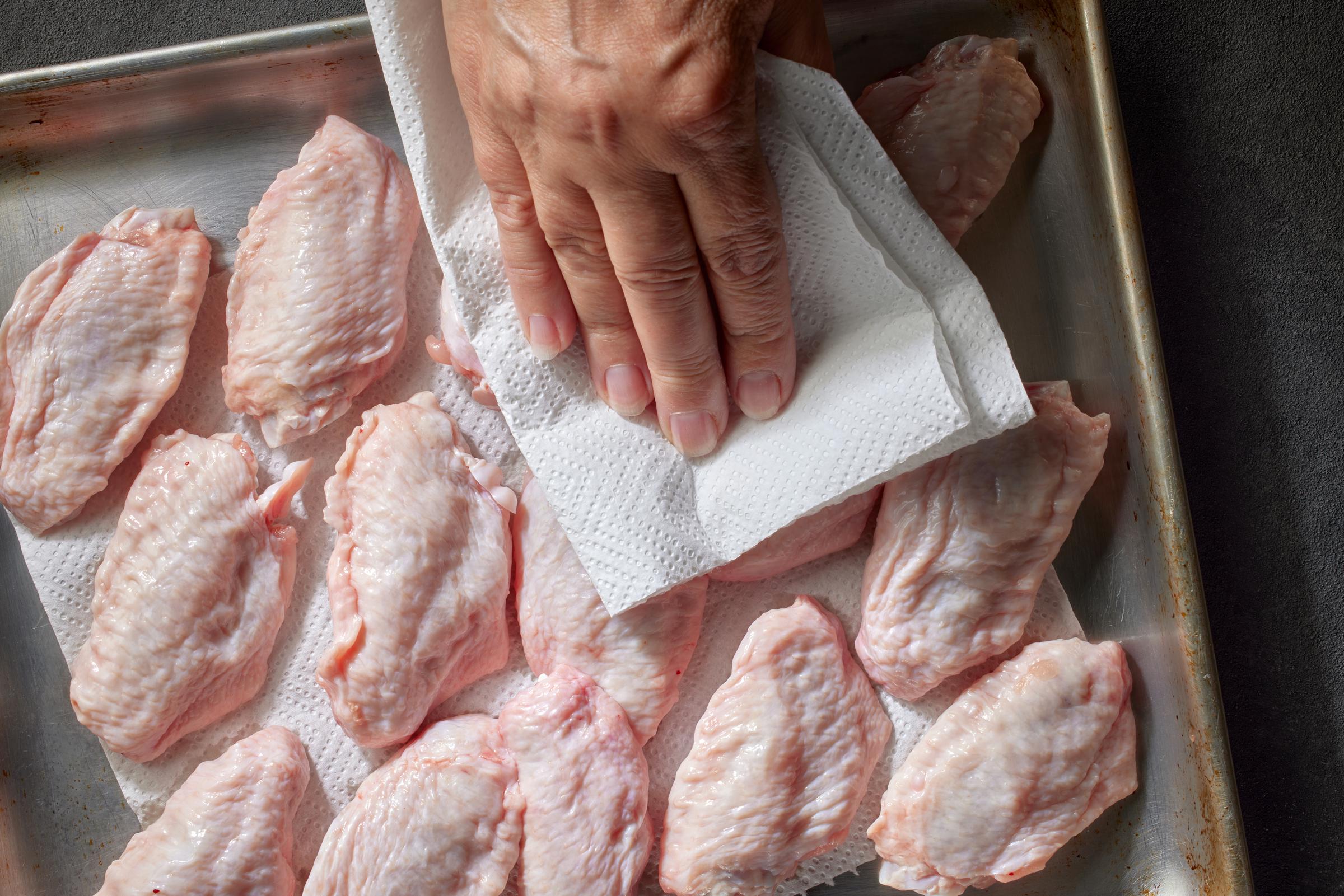 A woman patting her chicken wings dry with a paper towel | Source: Getty Images