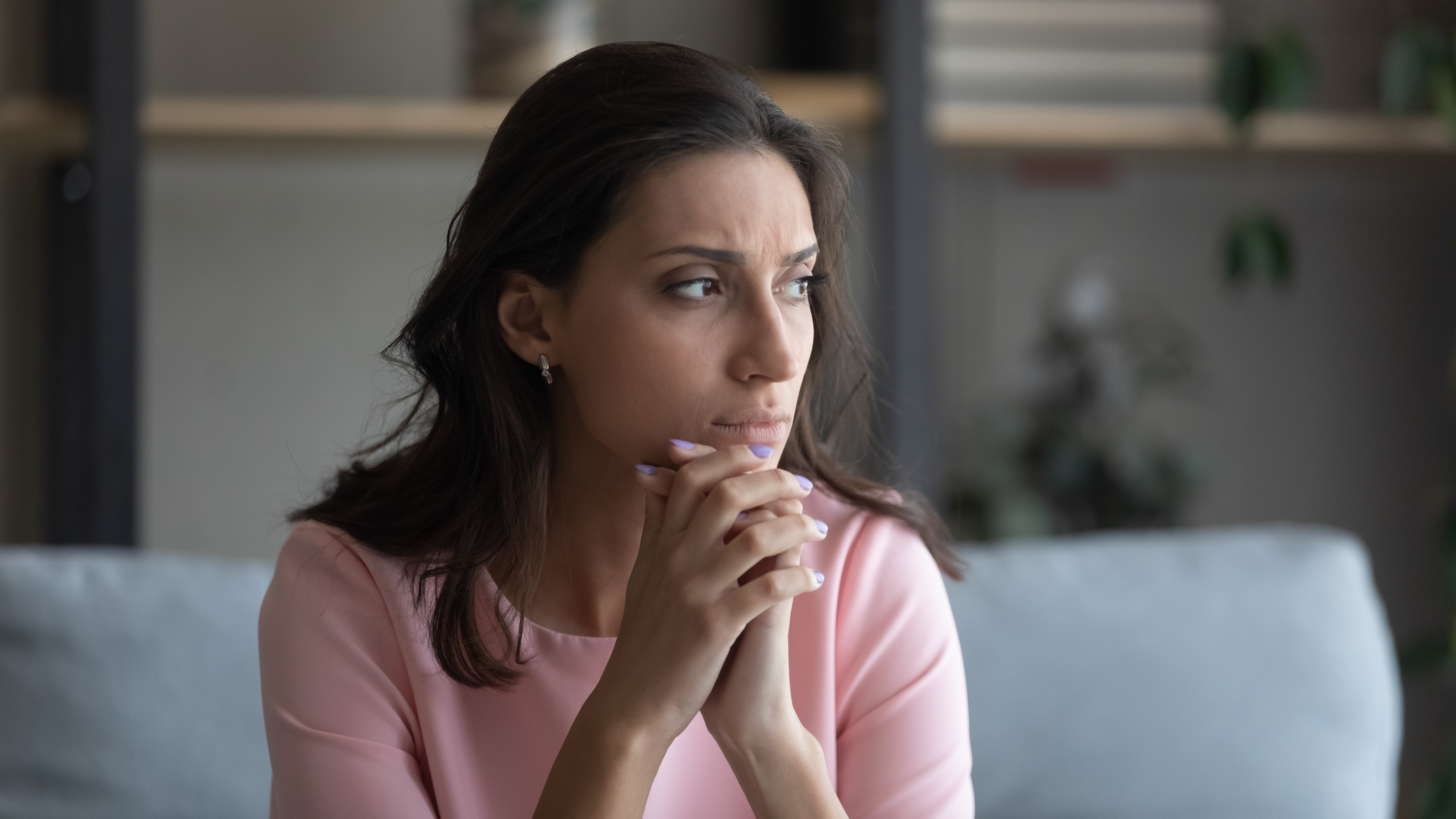 Pensive woman looking out the window while sitting on the sofa | Source: Shutterstock