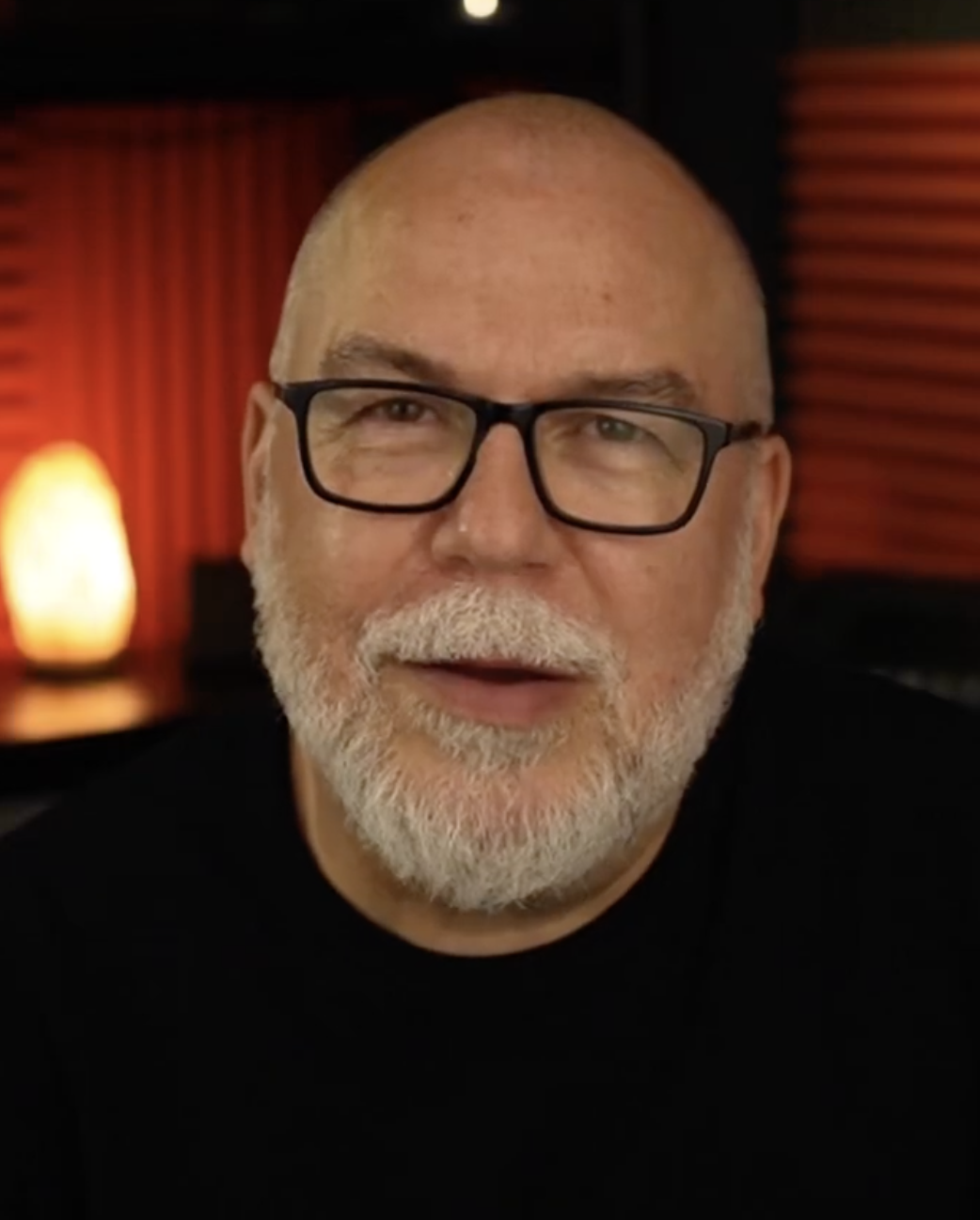 Now fully bald and white-bearded, Brookstein stares into the camera with a measured expression in a still from a July 2025 YouTube video, a salt lamp glowing warmly to his left — older, but settled and self-possessed. | Source: YouTube/stevebrookstein