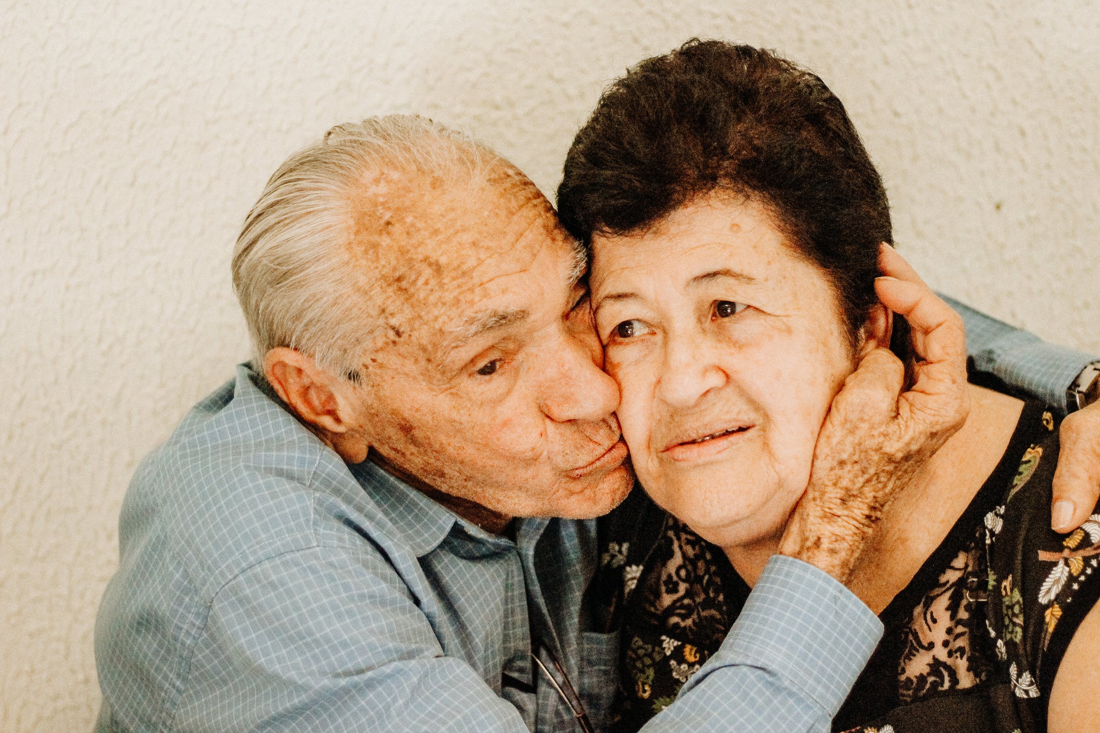 Anciano besando a su esposa mientras la abraza. | Foto: Pexels