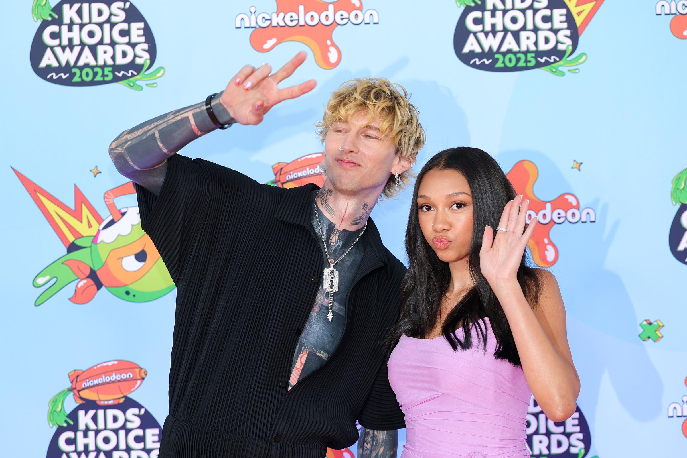 In sync and playful, MGK and Casie Baker flash matching peace signs for the cameras. Their fun-loving energy sets the tone at the Nickelodeon Kids' Choice Awards on June 21, 2025.