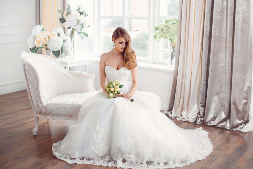 A photo of bride in beautiful dress sitting on sofa indoors. | Photo: Shutterstock