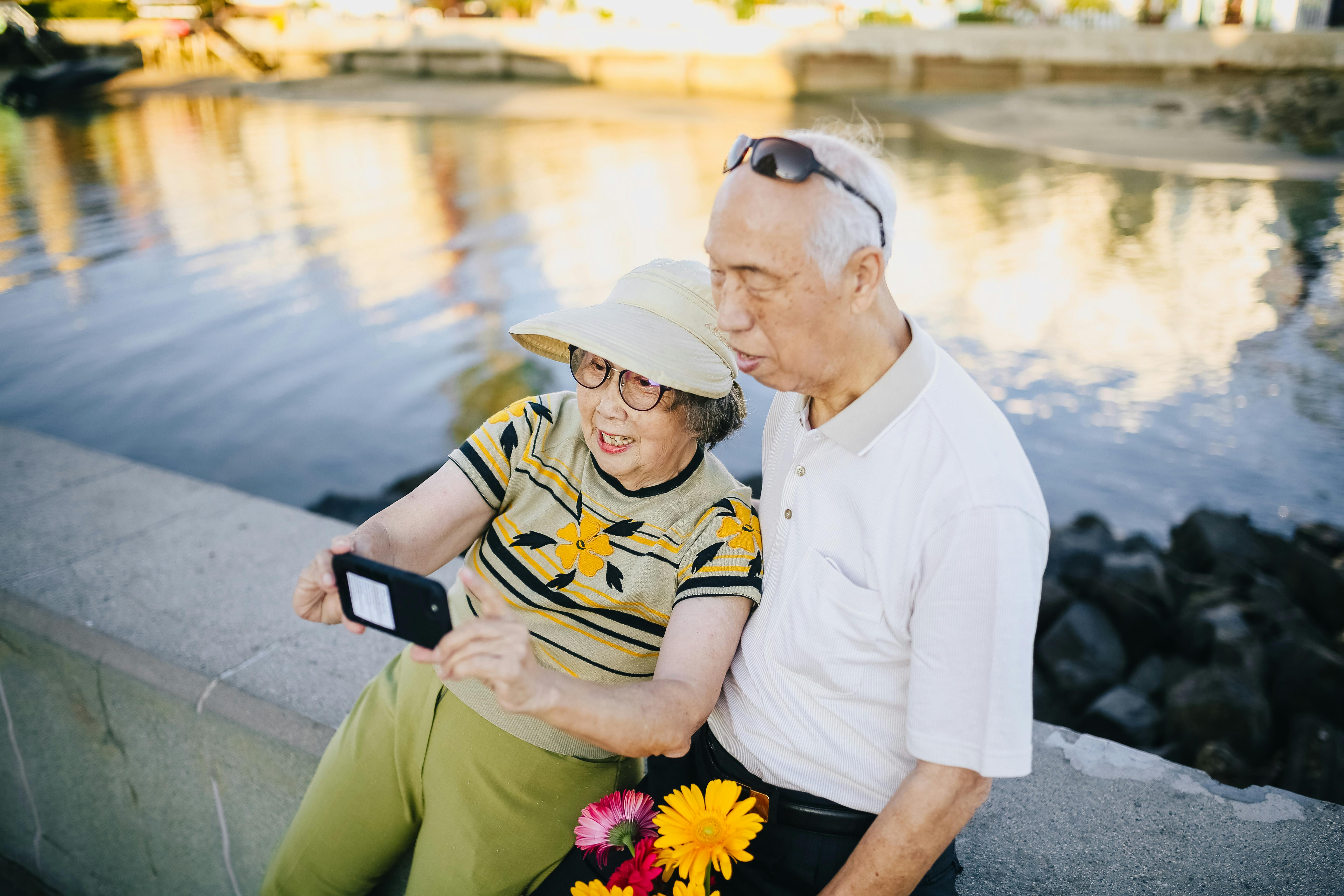 Elderly couple on concrete bench taking a selfie | Source: Pexels