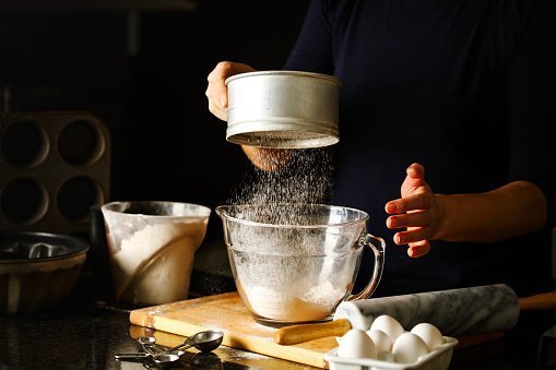 Woman sifting flour through sieve | Photo: Getty Images