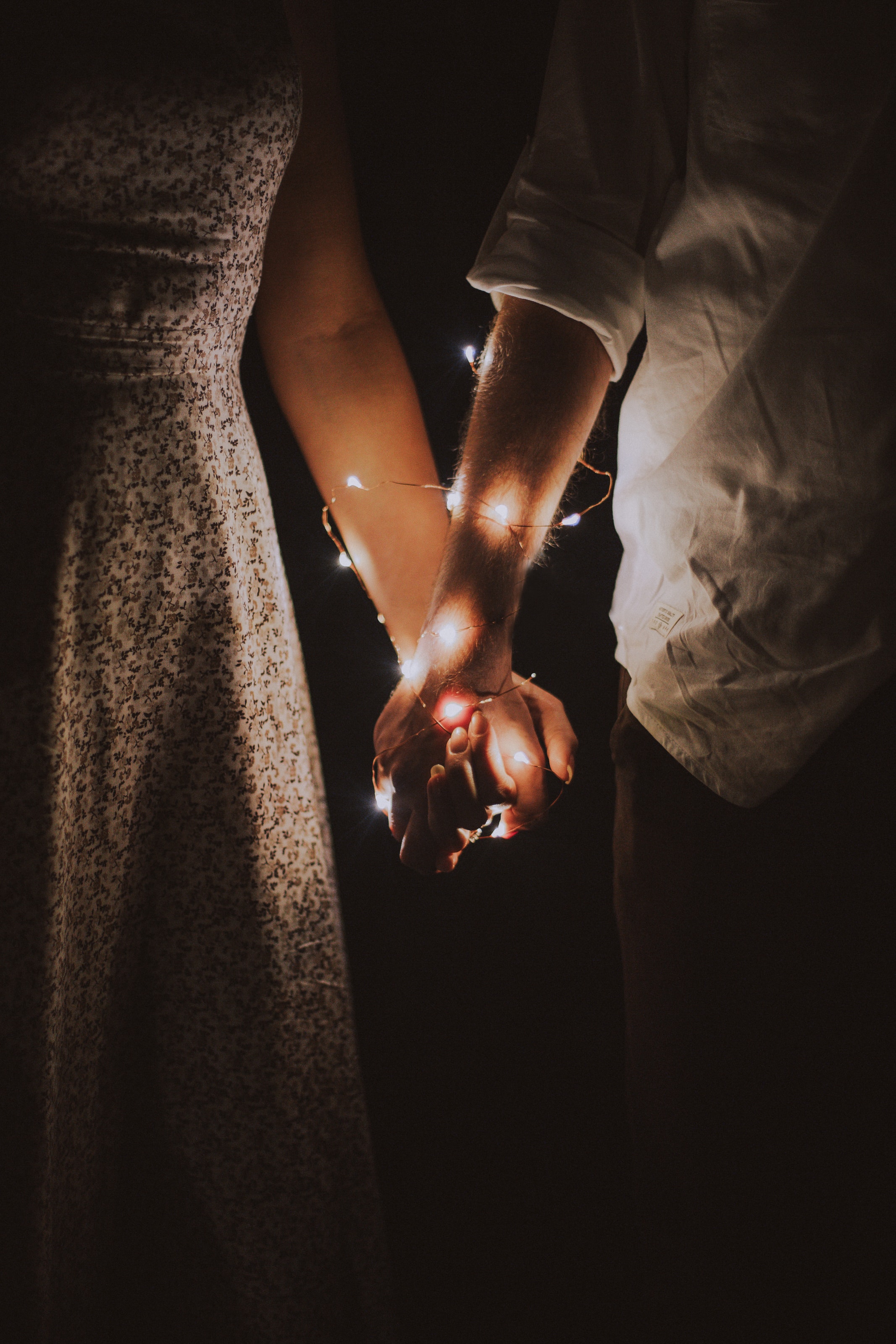 Man and woman holding each others hand wrapped with string lights. | Source: Pexels