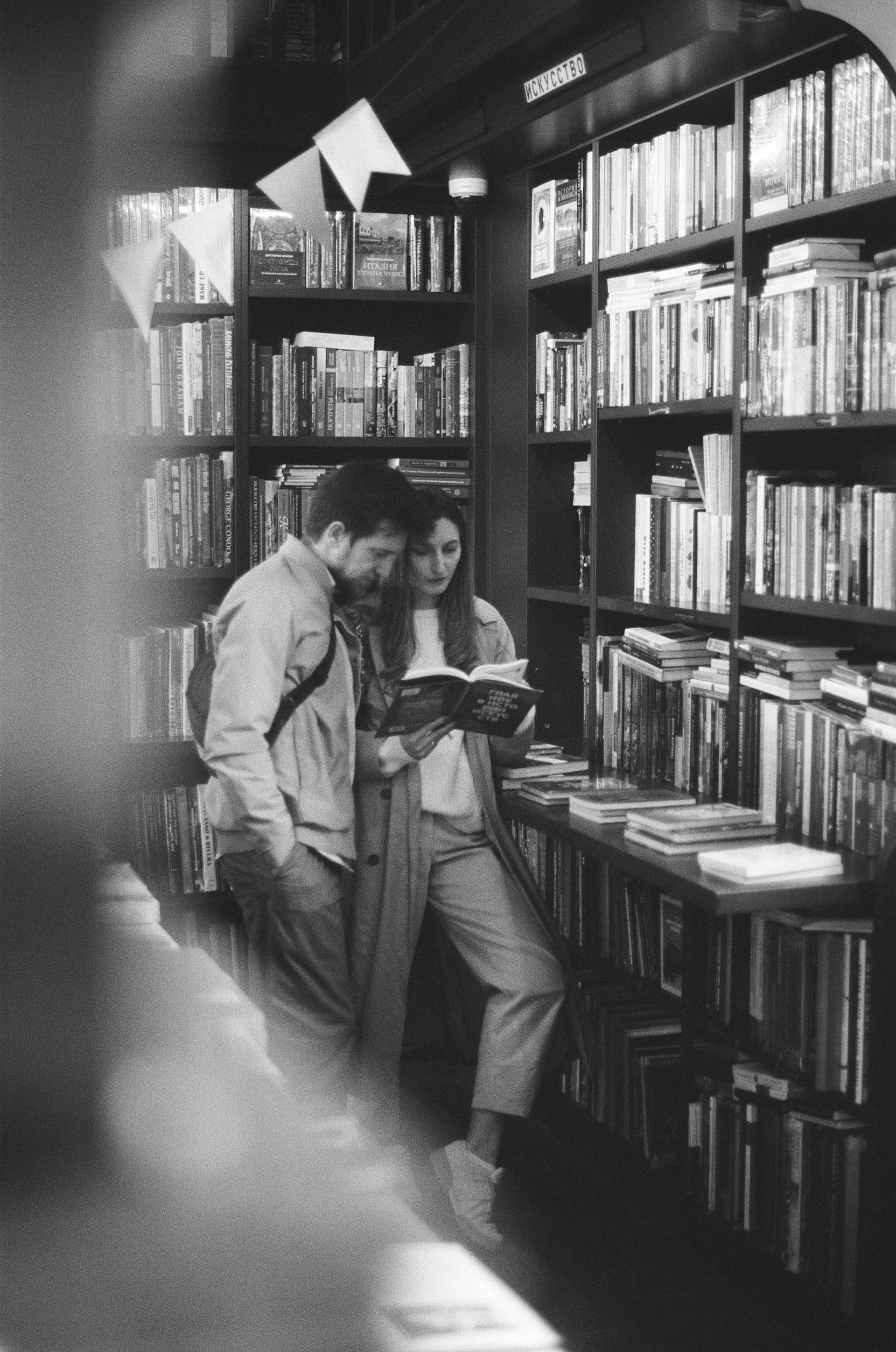 A grayscale photo of a couple reading a book in a library | Source: Pexels