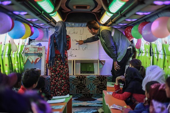 A Syrian teacher interacts with a Syrian child inside a bus which is converted into a classroom | Photo: Getty Images
