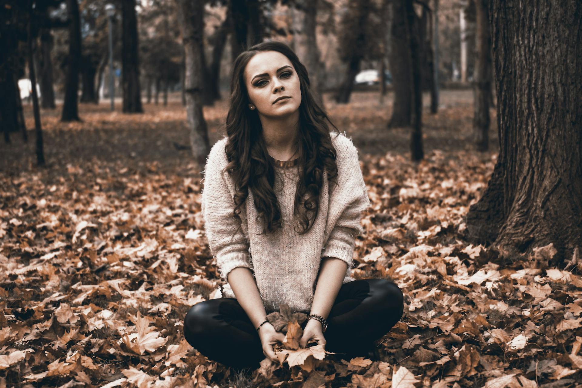 A young woman sitting in a forest holding fallen leaves | Source: Pexels