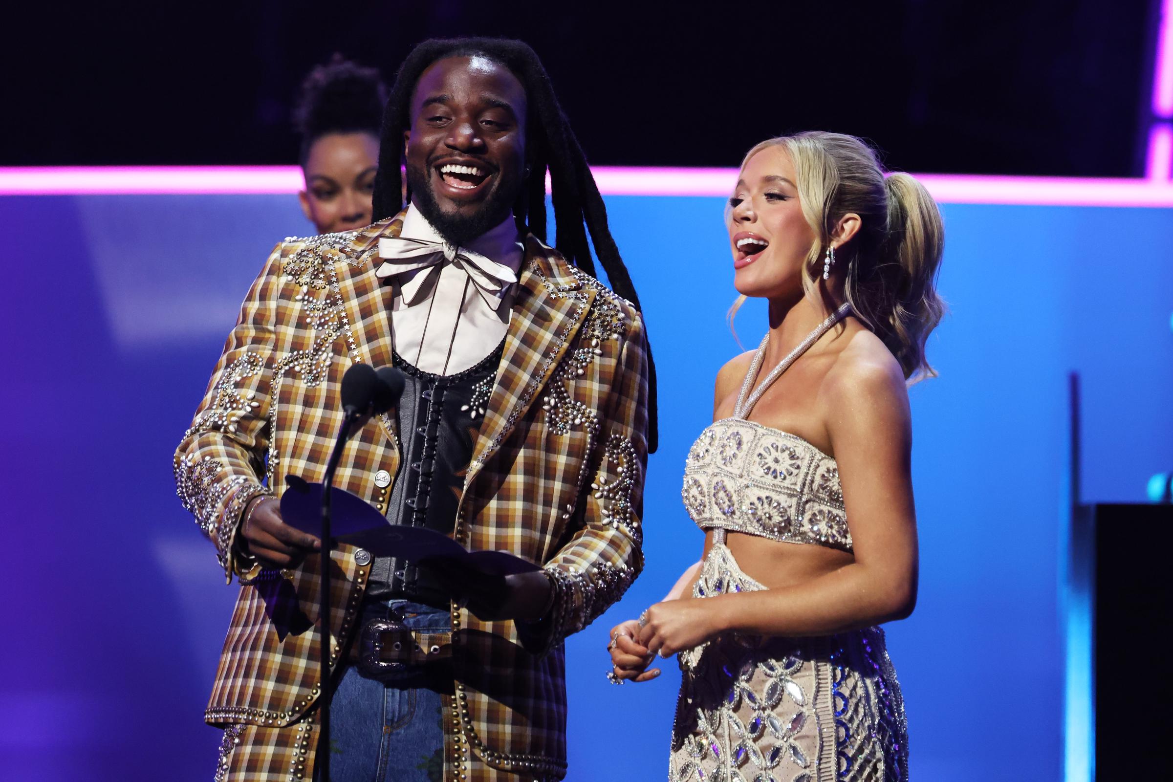 With mics in hand and laughter on their faces, the dynamic presenting duo delivers charm and chemistry under the show’s electric purple lights.
