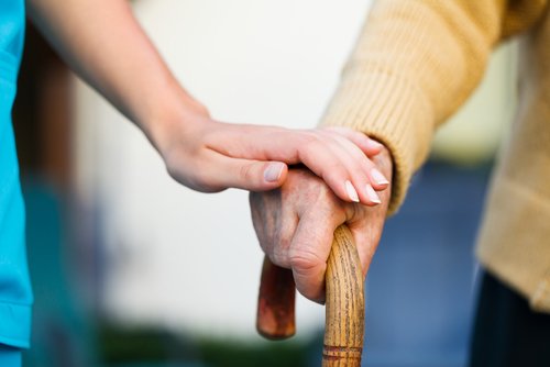 Enfermera con la mano puesta sobre un adulto mayor que se apoya en su bastón. | Foto: Shutterstock.com