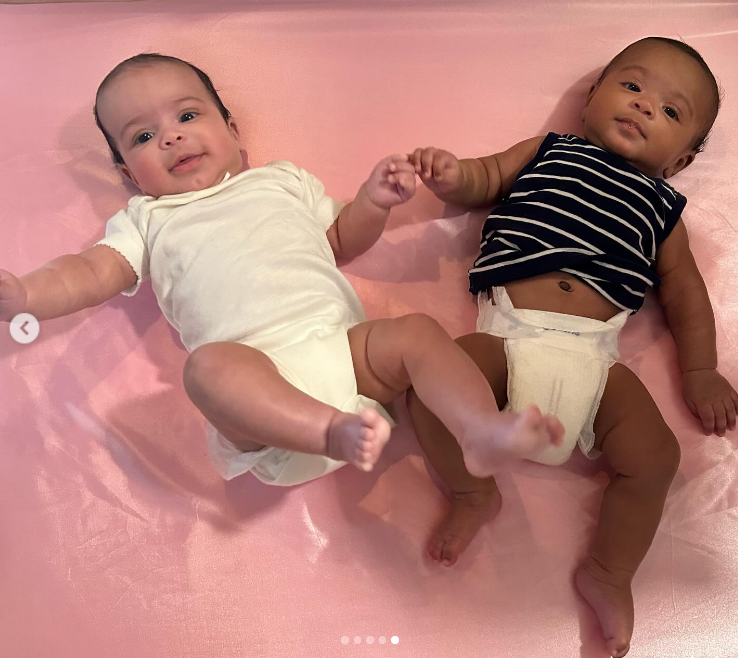 A photo of Maya in an all-white onesie and Cooper in a striped black shirt and diaper, lying on a pink blanket, posted in August 2024 | Source: Instagram/brandontour