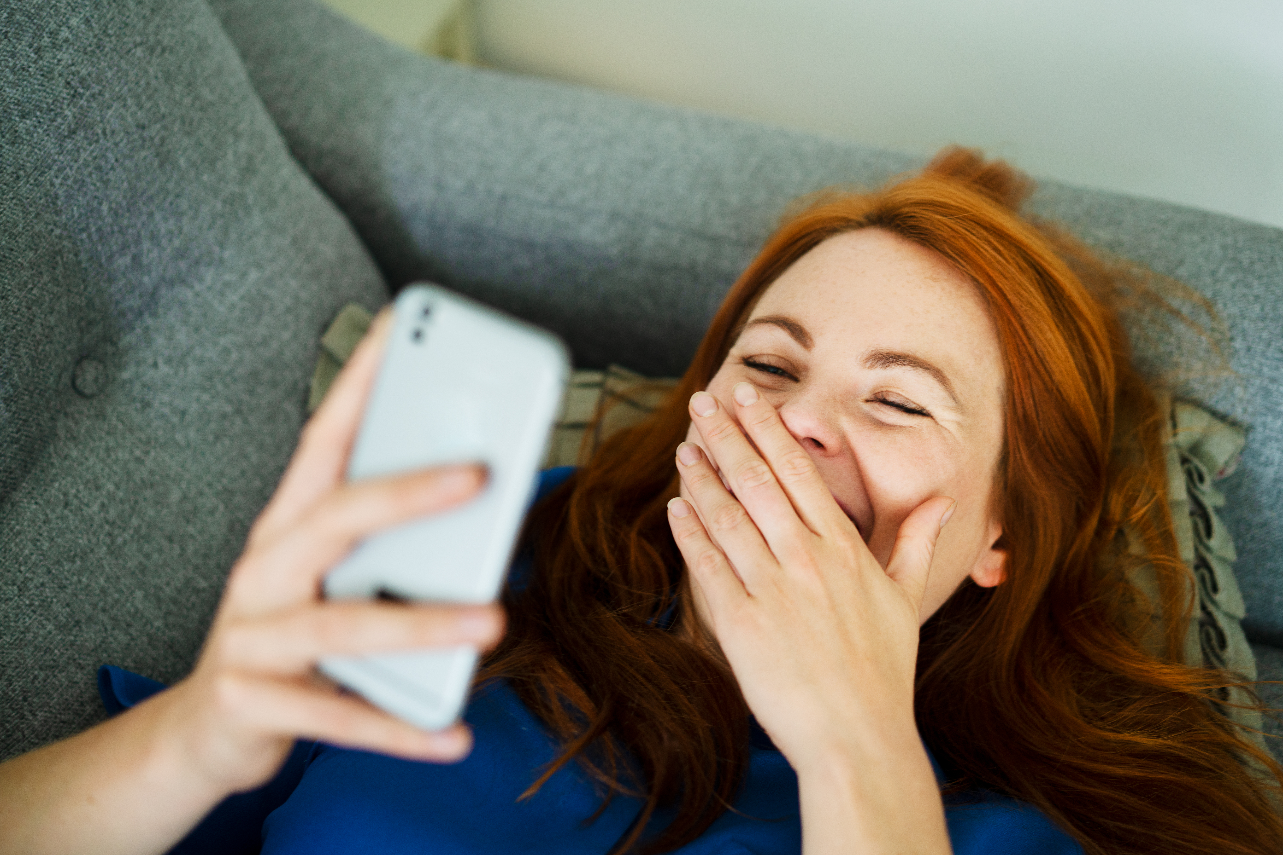 A woman laughing at her phone while lying on the sofa | Source: Getty Images