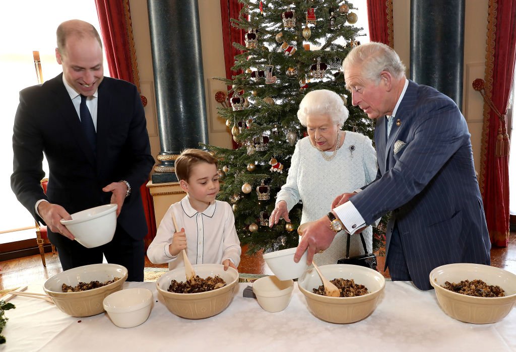 Prince William, Duke of Cambridge, Prince George, Queen Elizabeth II and Prince Charles, Prince of Wales prepare special Christmas puddings in the Music Room at Buckingham Palace, as part of the launch of The Royal British Legion's Together at Christmas initiative. | Photo: Getty Images