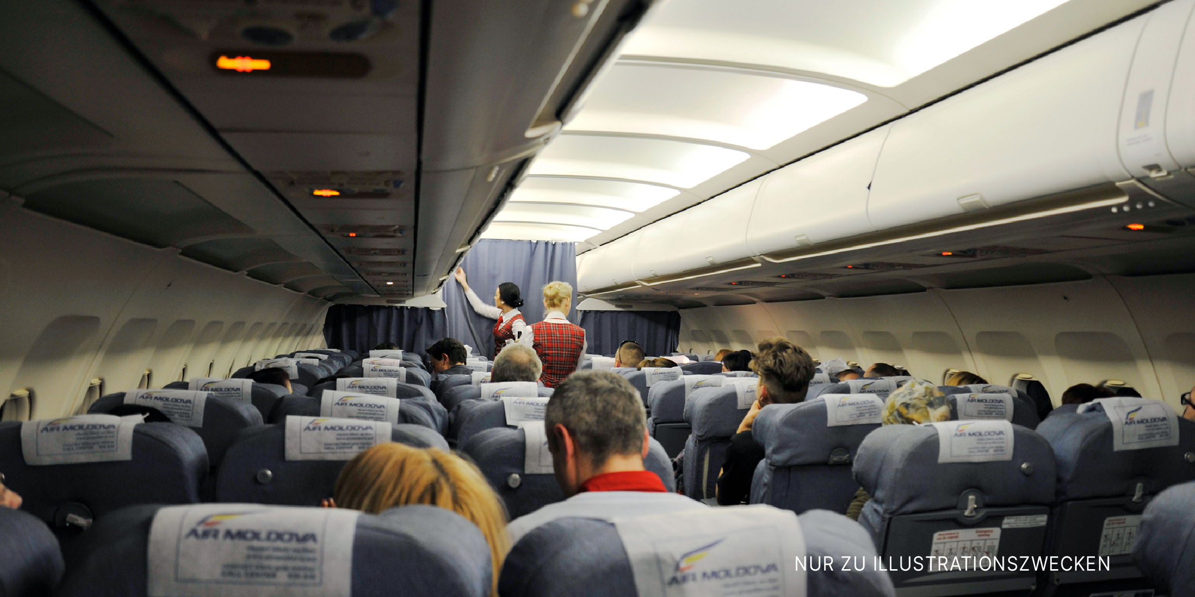 Innenraum eines Flugzeugs mit sitzenden Passagieren und Flugbegleitern | Quelle: Shutterstock