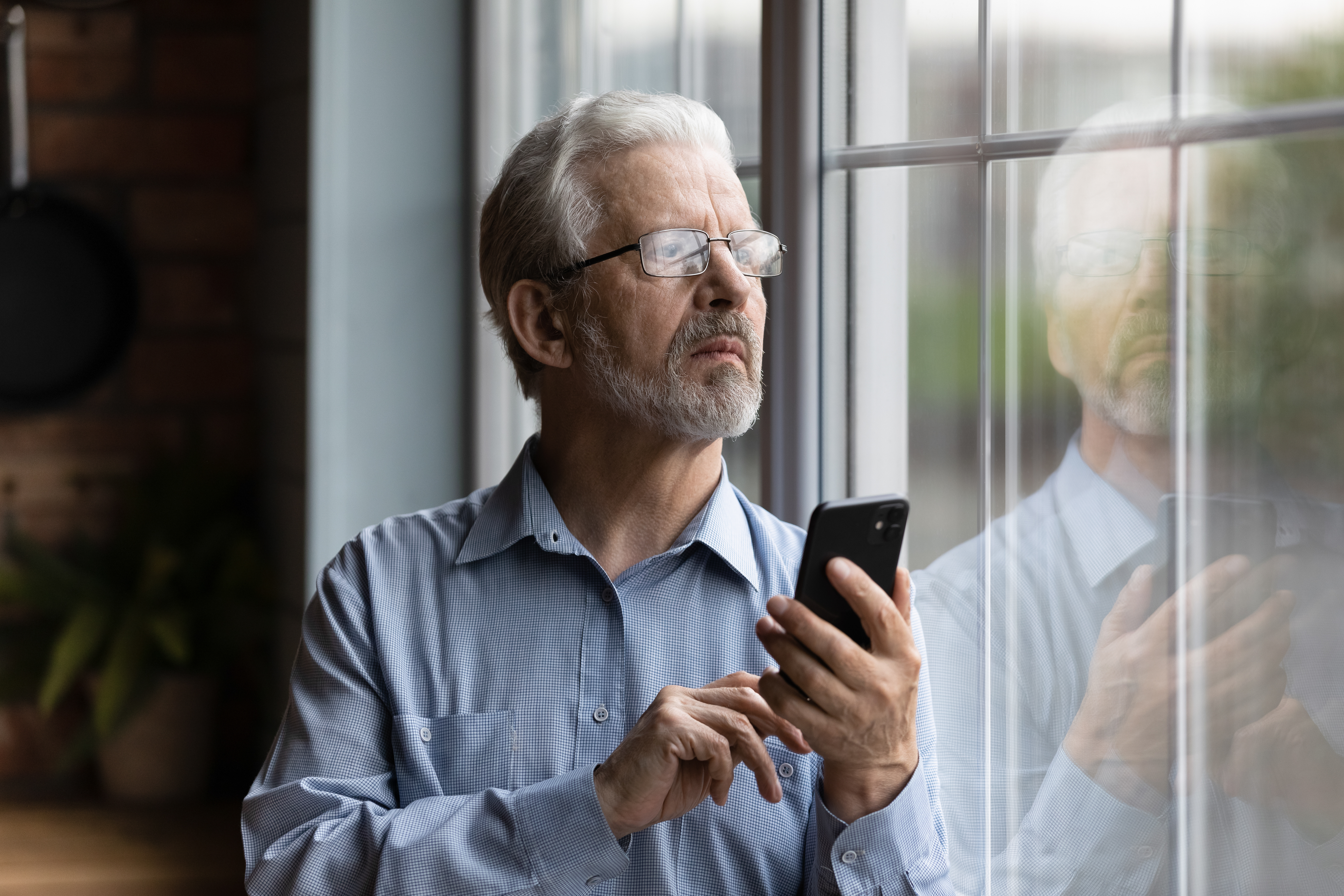 A man looking outside a window with a phone in his hand | Source: Shutterstock