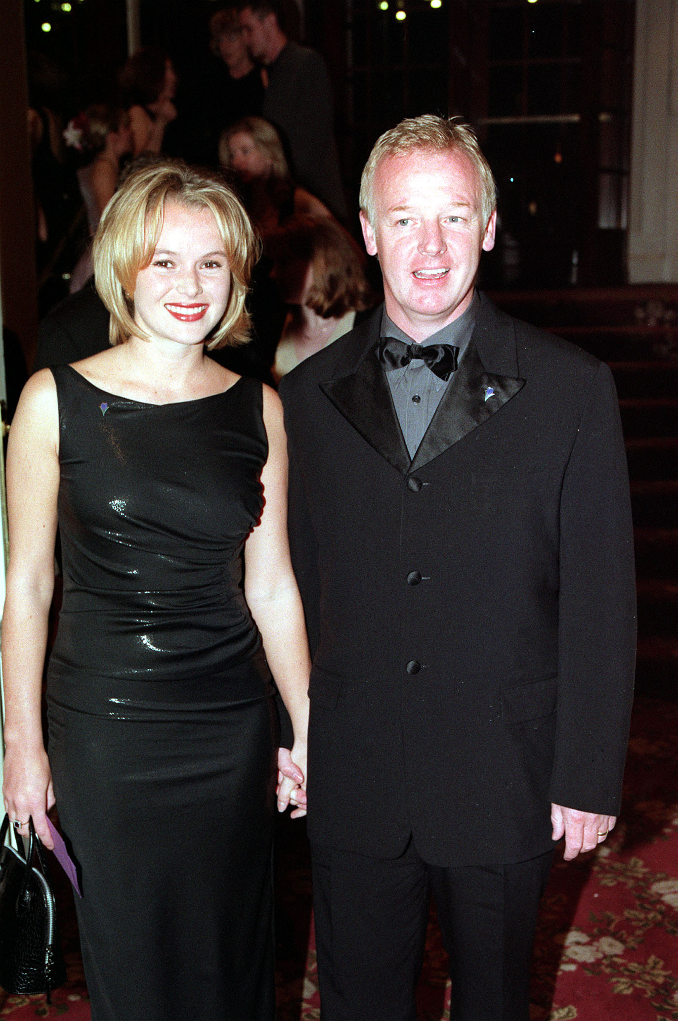 Dennis, in a black tuxedo with satin lapels, and Holden, in a black satin ruched midi dress, pose together on the red carpet at the TV Quick Awards at the Grosvenor House Hotel in London.