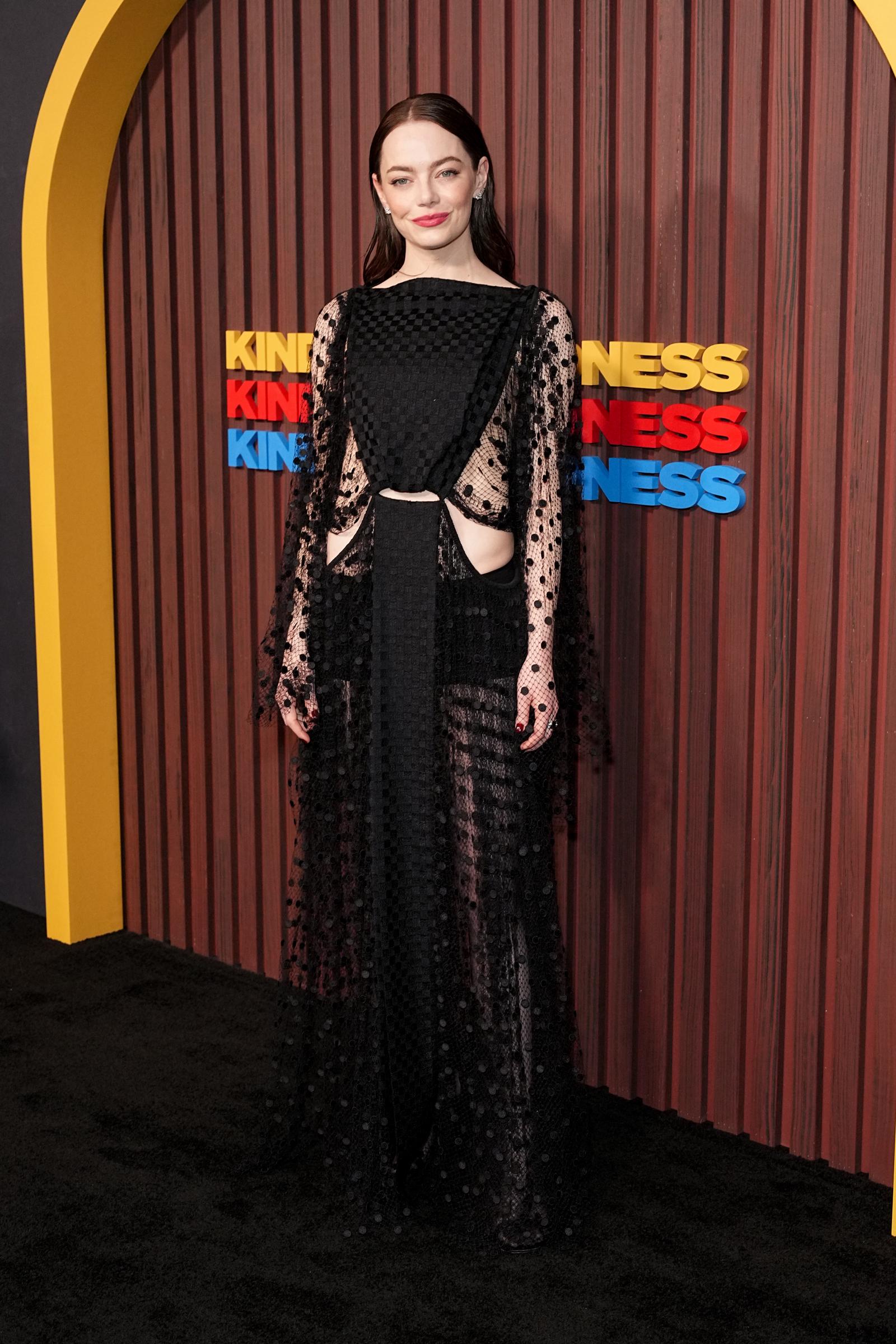 The actress attended the “Kinds of Kindness” premiere in New York wearing a sheer black polka-dot gown with cutout panels at the waist and a checkerboard bodice. She kept her hair sleek and tucked behind the ears, finishing the look with bold pink lipstick and dark nails.