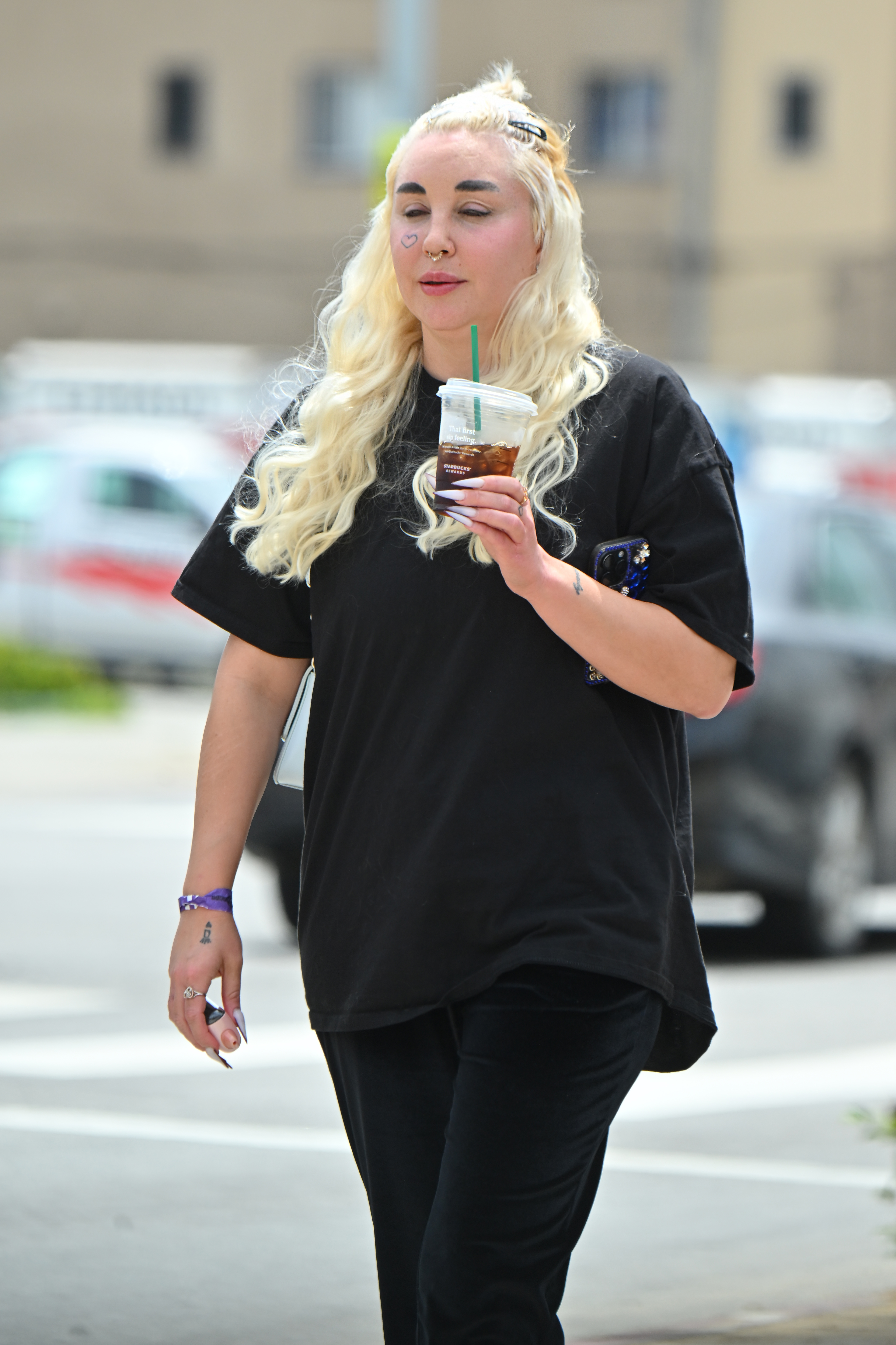 Spotted in Los Angeles, Amanda Bynes strolls with a cold drink in hand, sporting platinum curls, dramatic brows, and a casual black tee—textured with edgy details that reflect her evolving style.