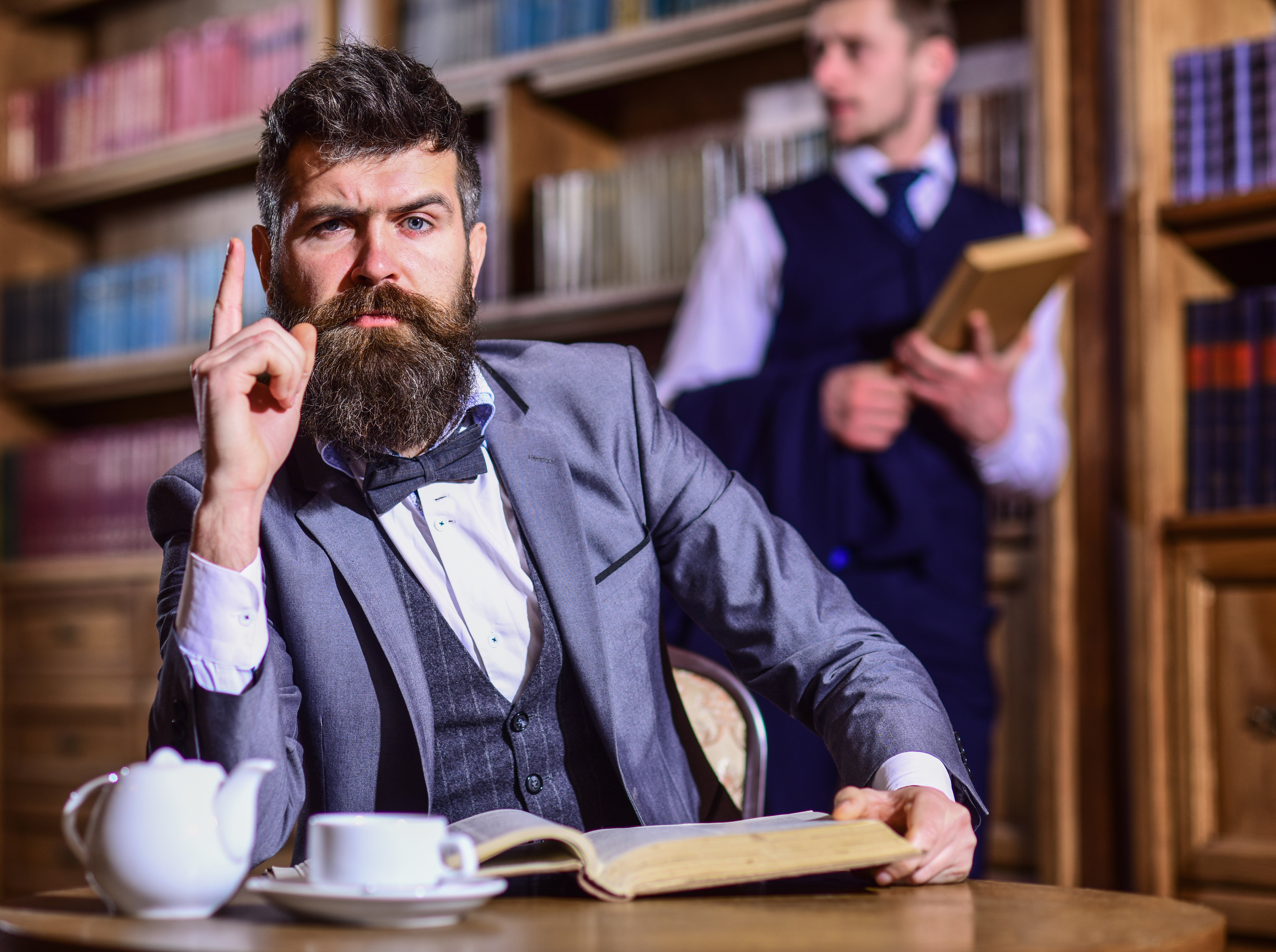 A man in a suit points one finger up as if he's figured a riddle while reading a book at the library | Source: Shutterstock