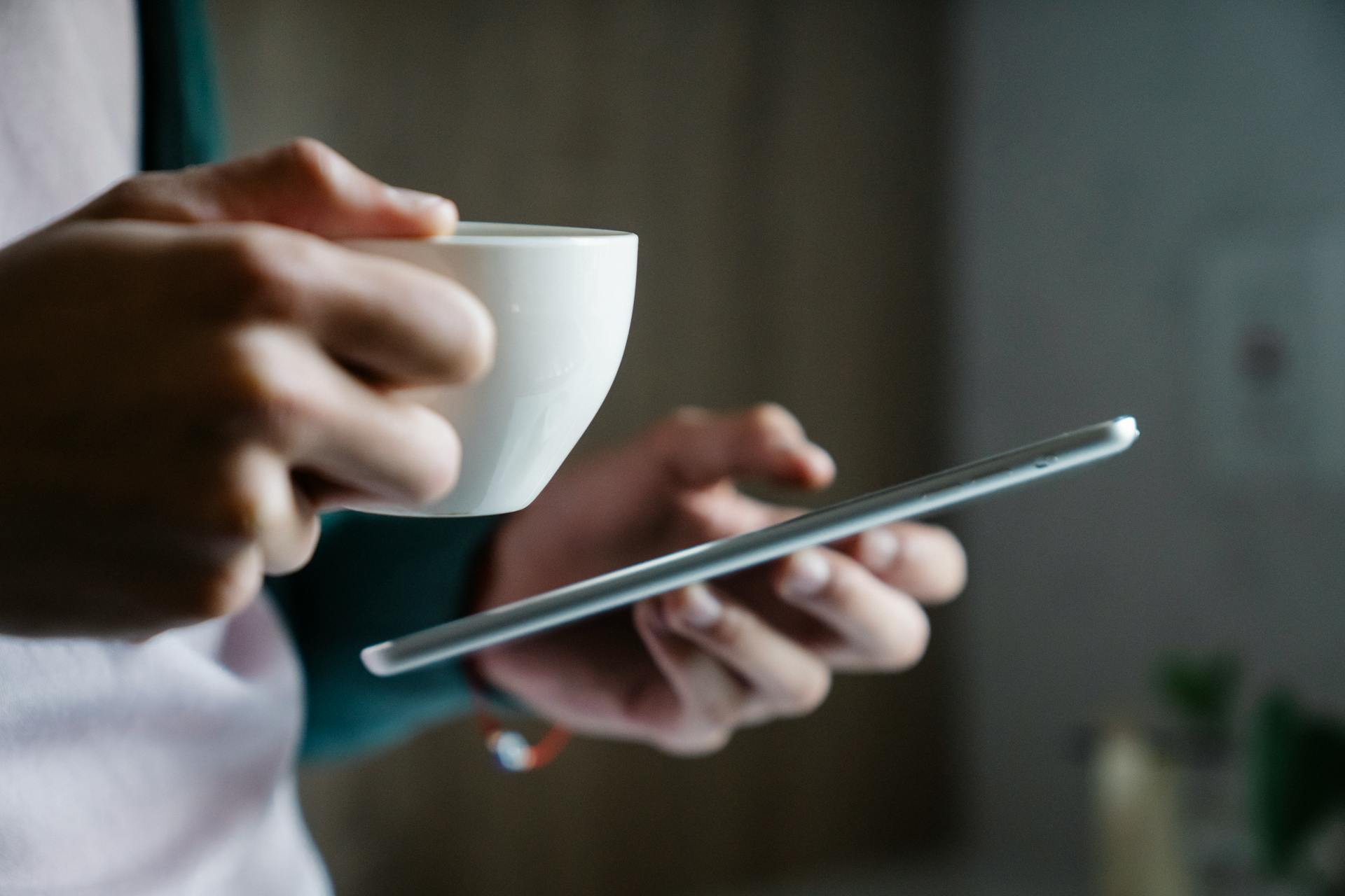 A closeup shot of a man holding a cup of coffee while using his smartphone | Source: Pexels