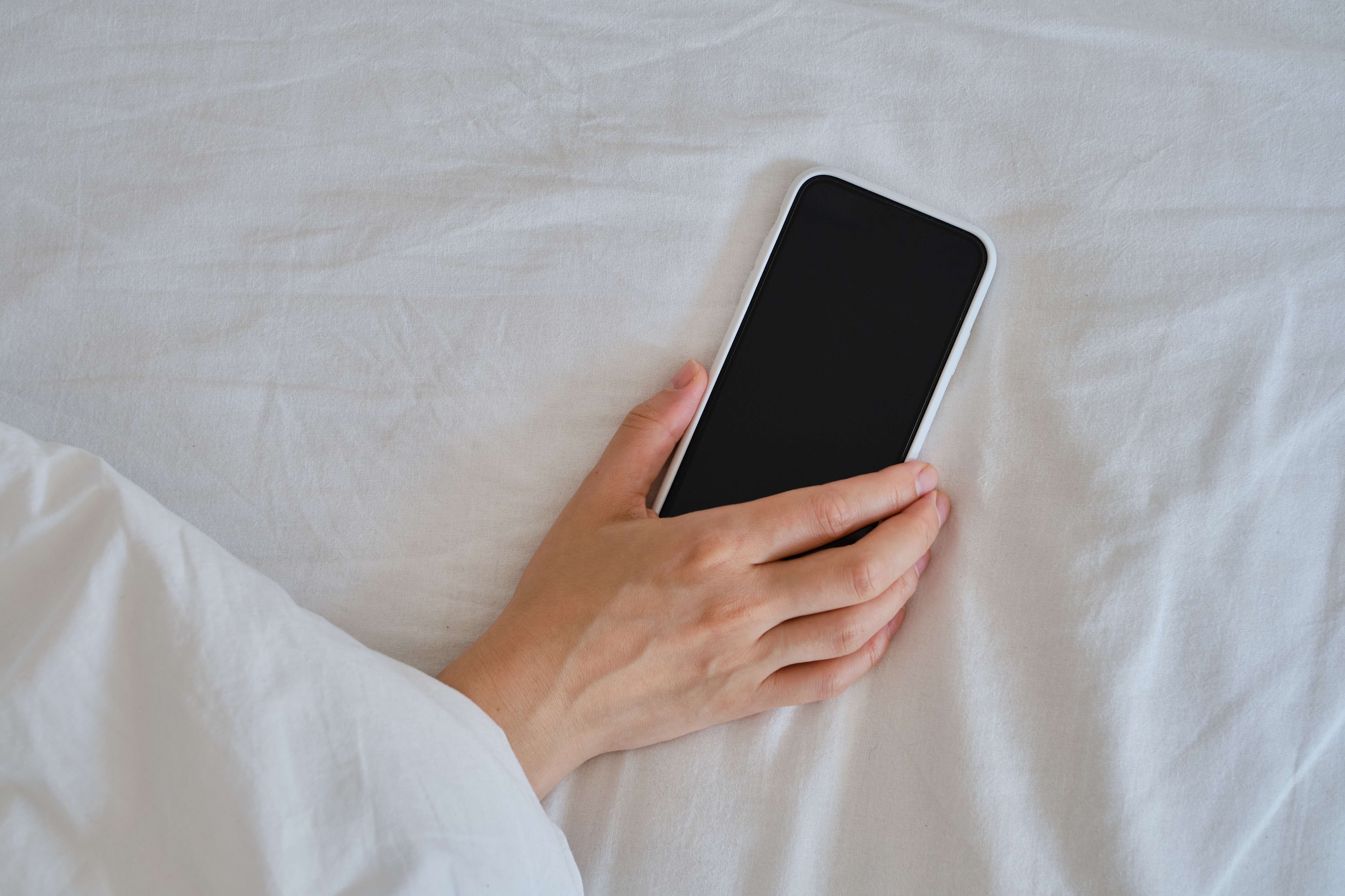 Close-up of a hand holding a smartphone in bed | Source: Shutterstock