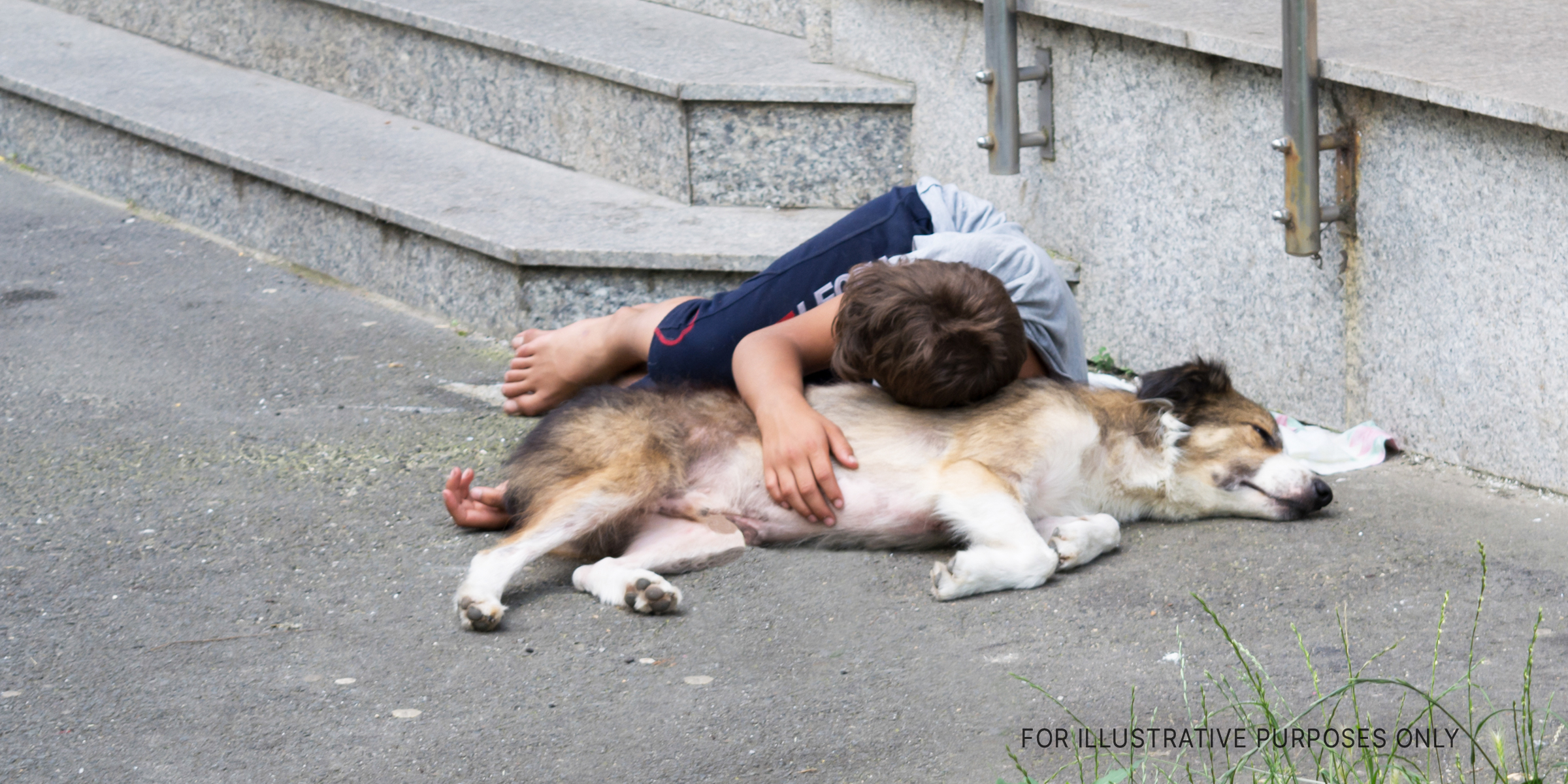 Boy lying on dog in street | Source: Shutterstock