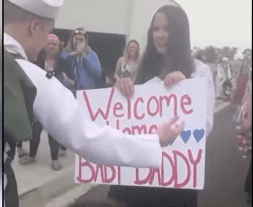 Natasha welcoming her husband Chris with a placard covering her baby bump. | Source: youtube.com/CBC Docs 