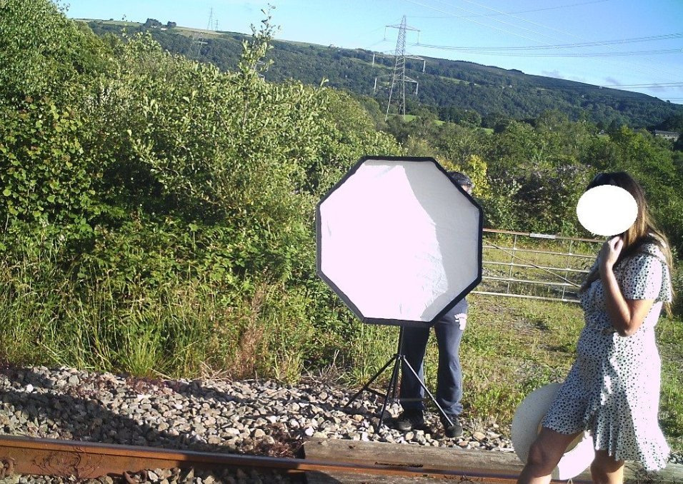 Woman walking on a railroad track while a man uses a studio light to take photographs of her. │ Source: twitter.com/WalesOnline