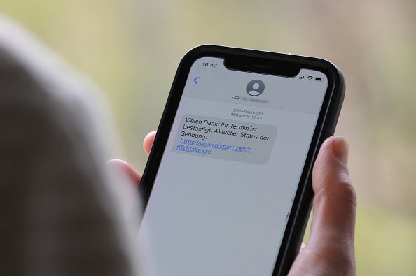 Une femme tient un smartphone dans sa main avec un SMS d'arnaque sur l'écran. | Photo : Getty Images